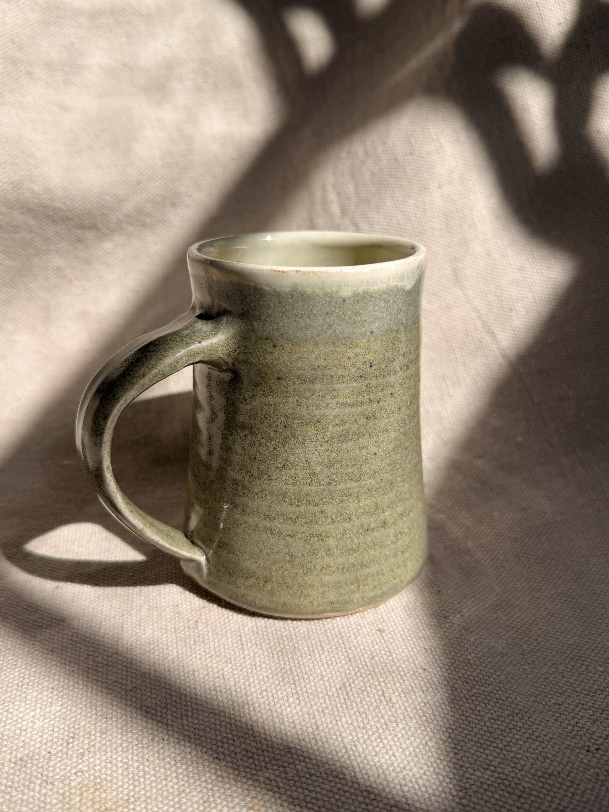 Green ceramic mug on a textured beige surface with shadows