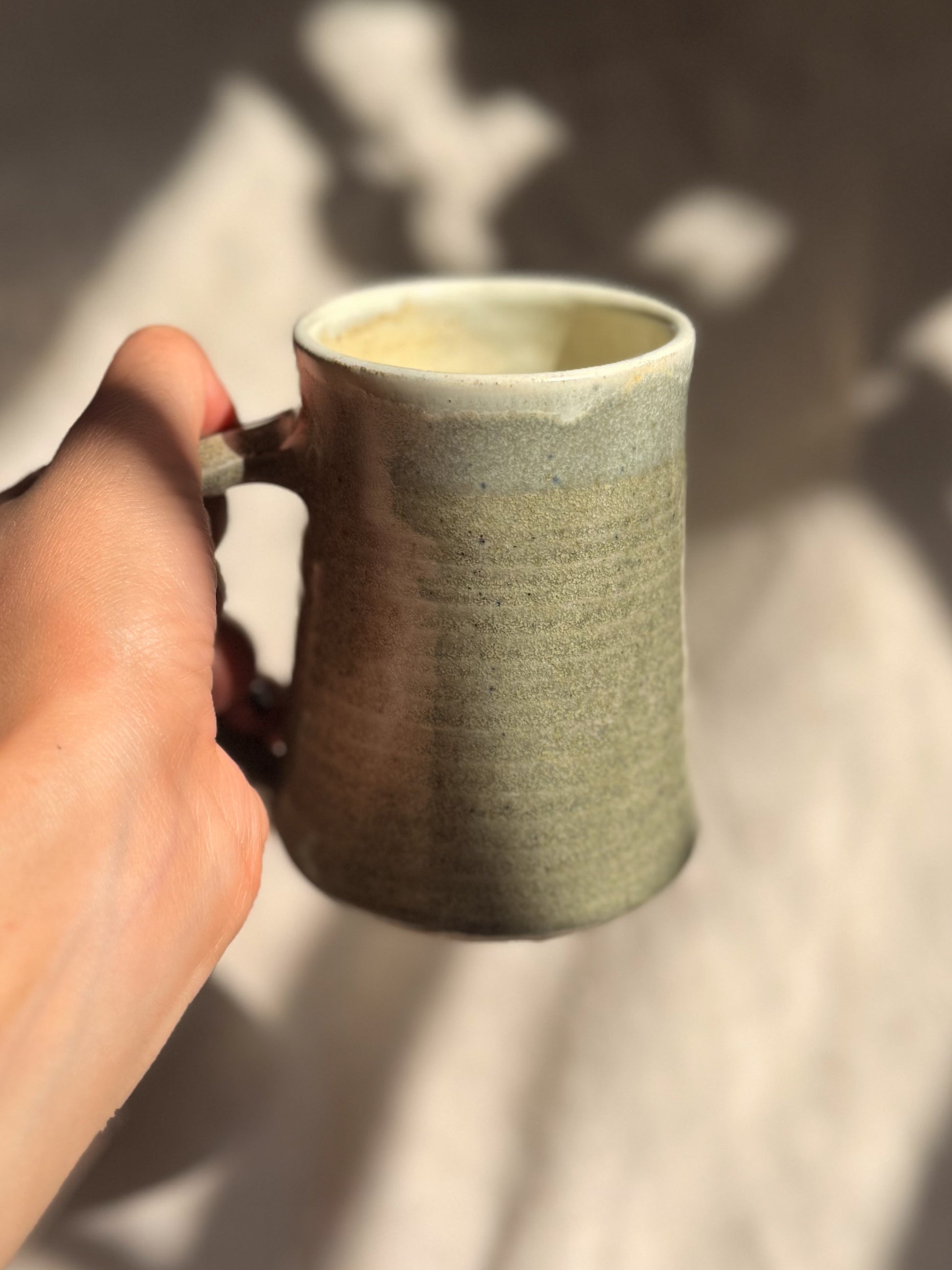 Hand holding a textured ceramic mug with steam rising, on a neutral background