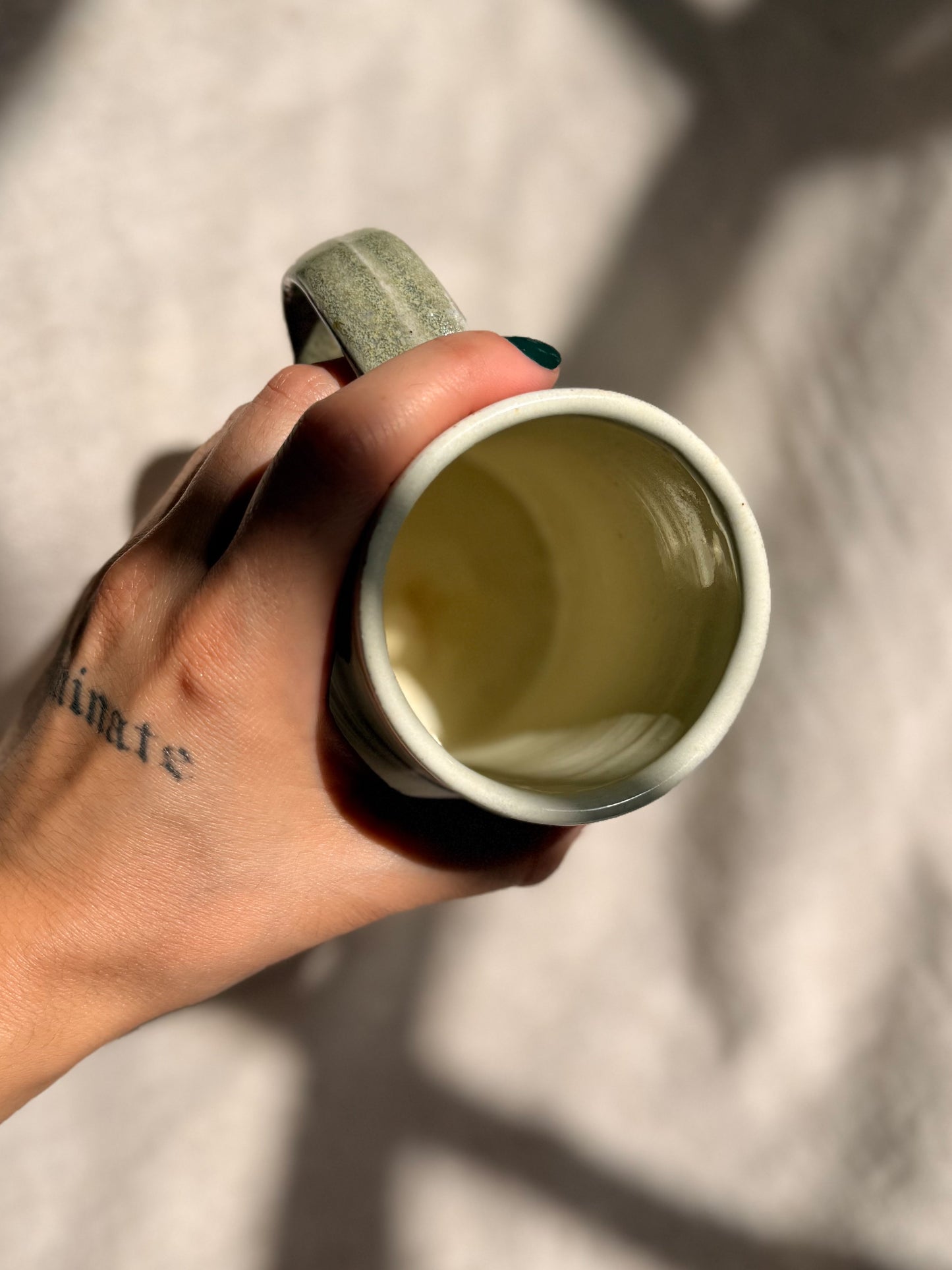 Hand holding a white mug with a green handle against a neutral background