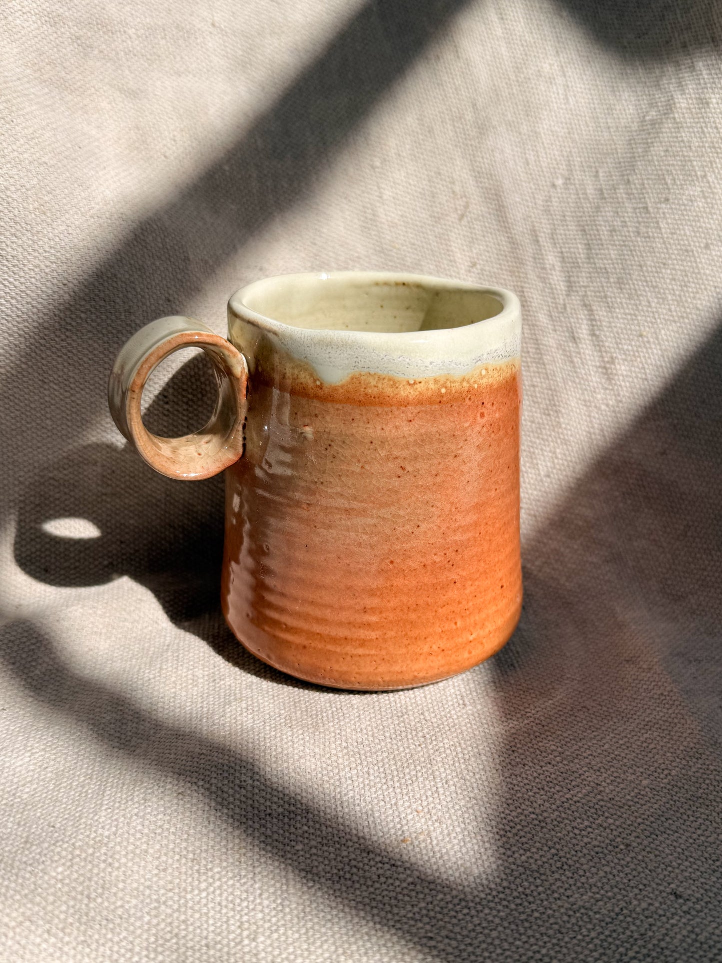 Ceramic mug with a gradient from beige to orange on a textured surface