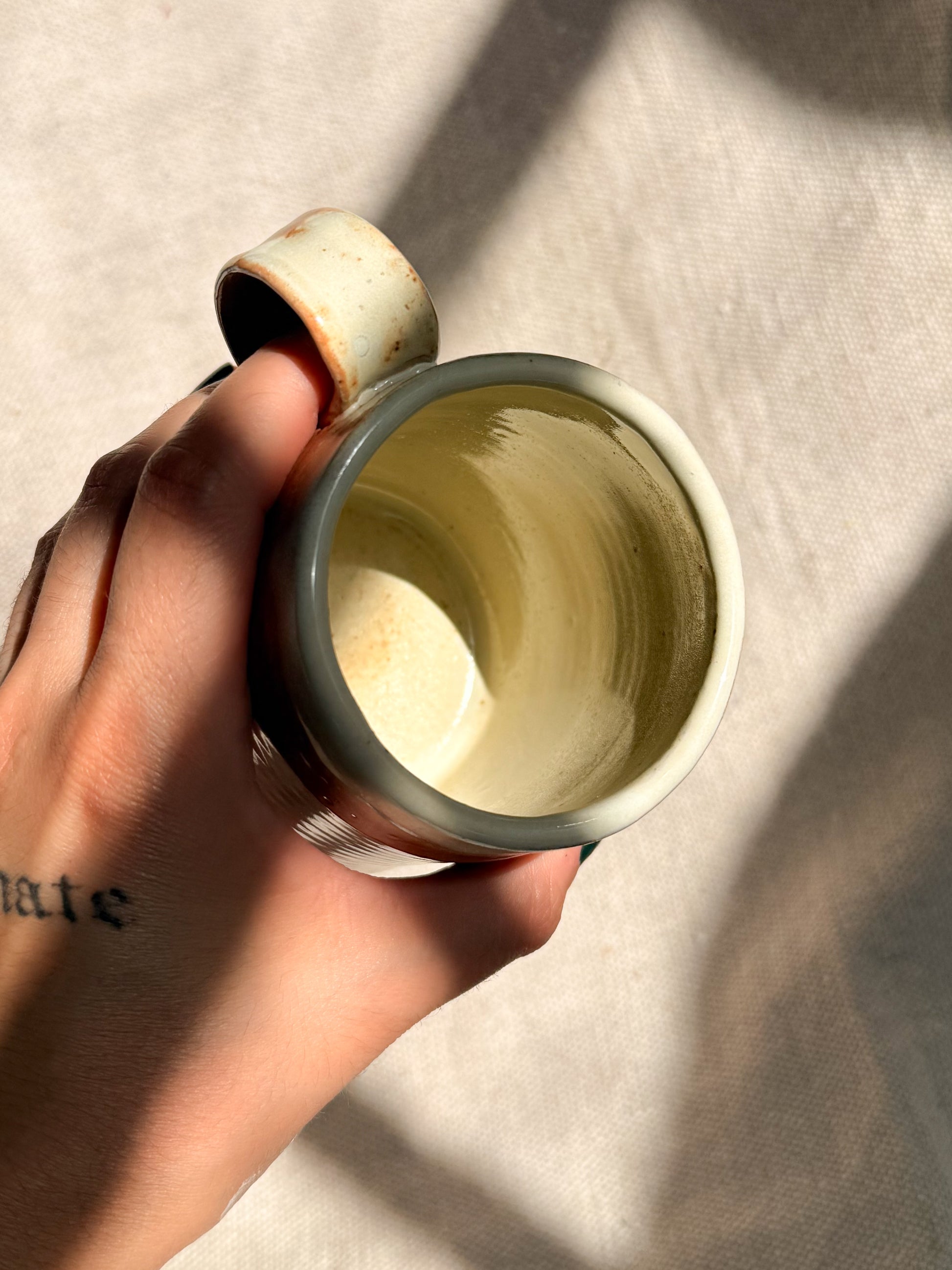 Hand holding a small ceramic cup with a textured interior against a neutral background