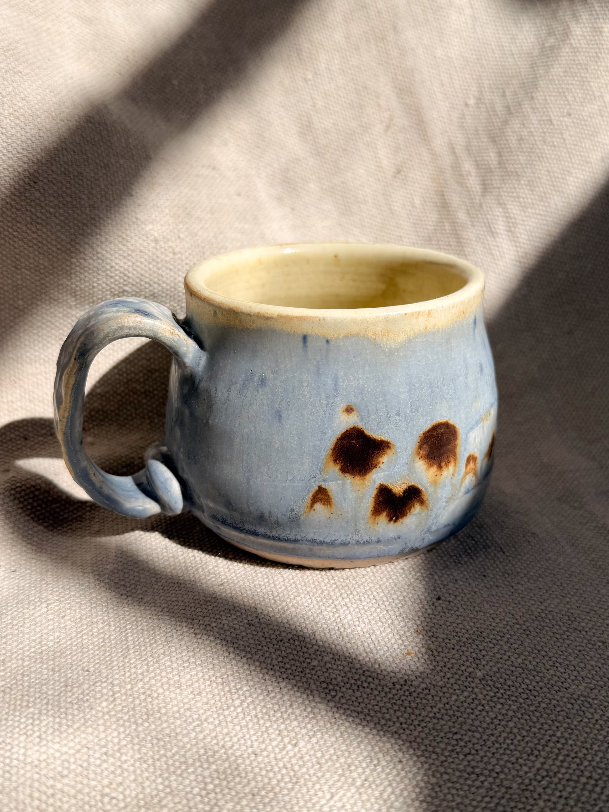 Ceramic mug with blue glaze and brown speckles on a textured fabric background