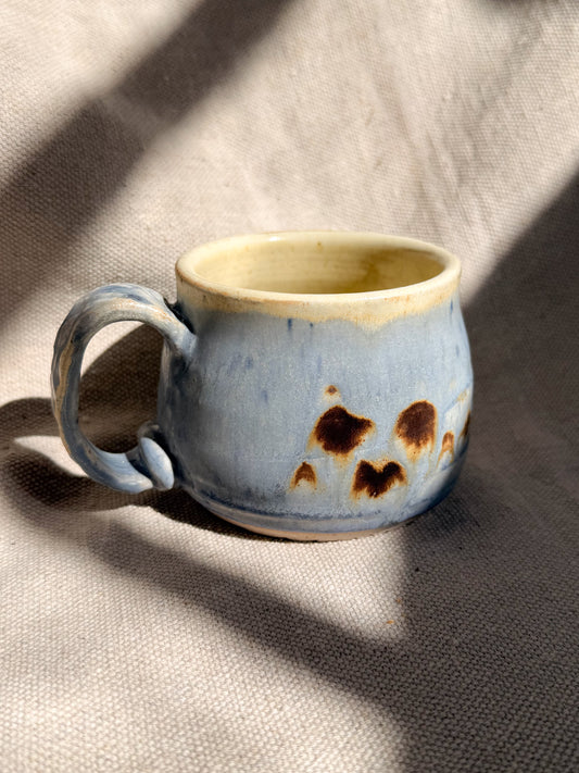 Ceramic mug with blue glaze and brown speckles on a textured fabric background