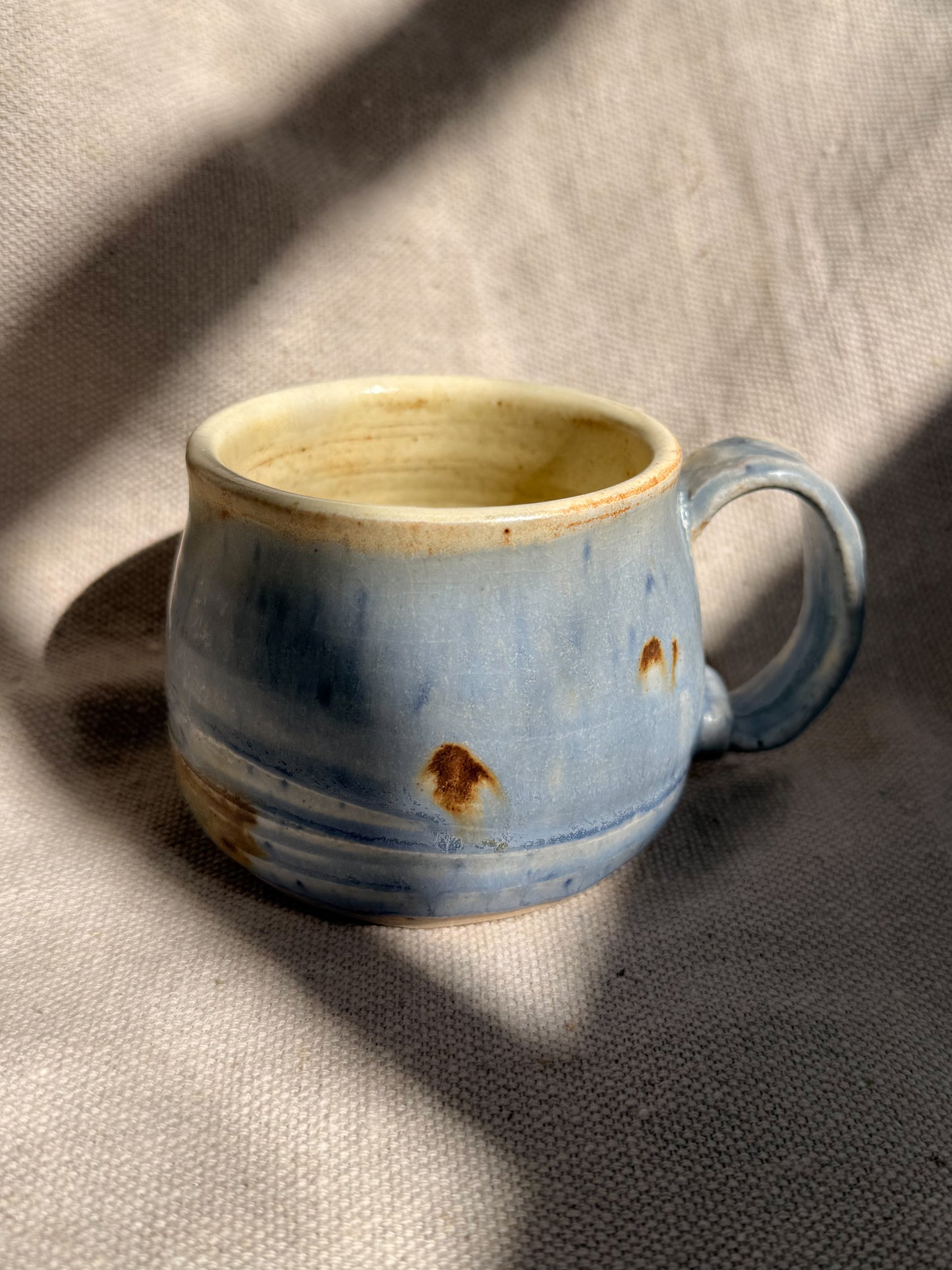 Blue ceramic mug with a handle on a textured beige surface
