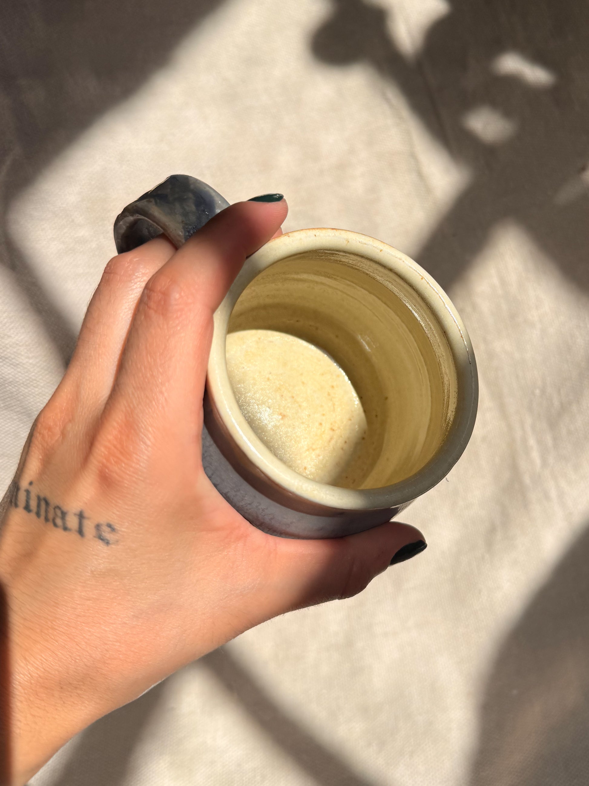 Hand holding a small ceramic container with a white substance on a light background