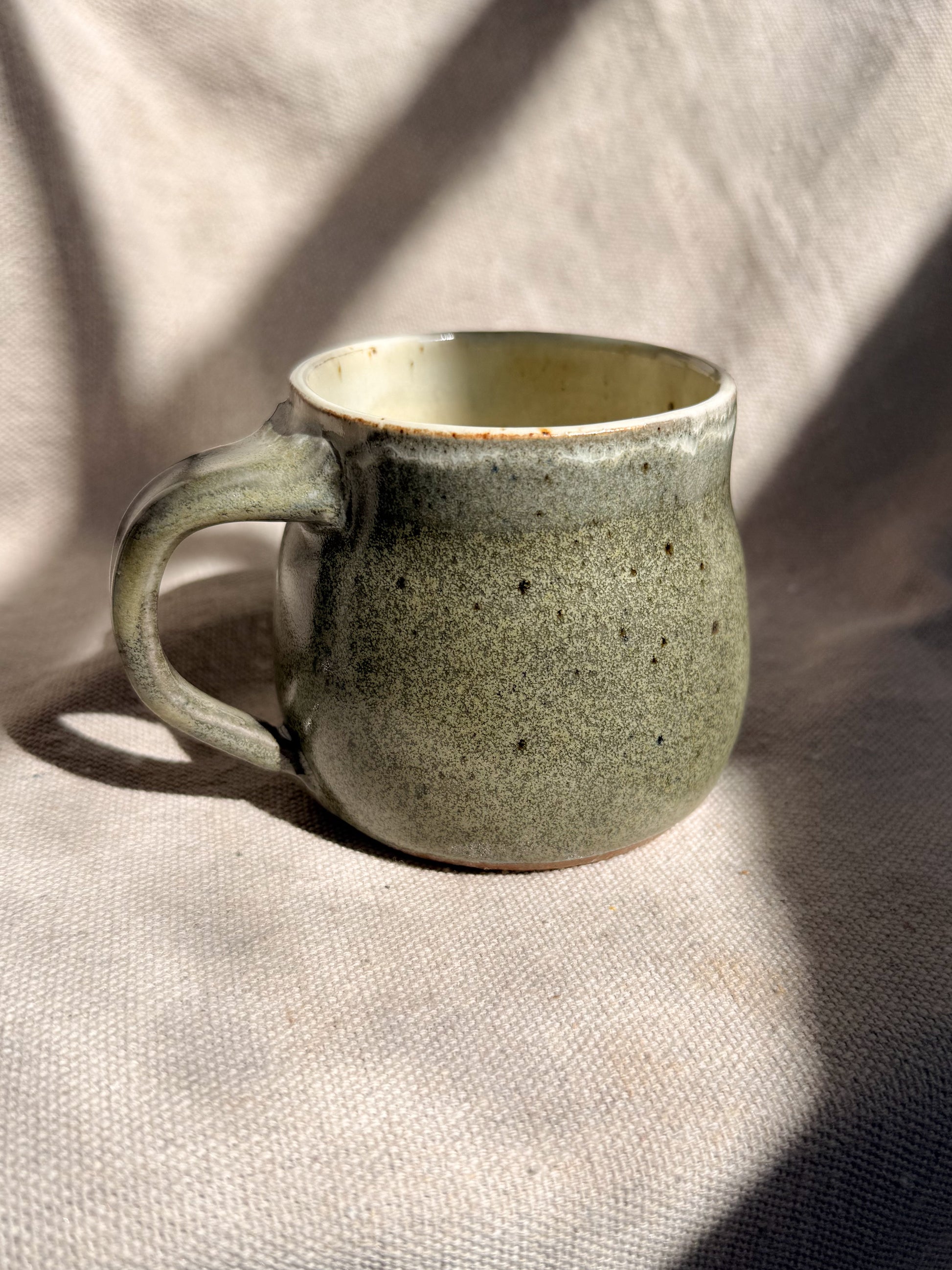 Green ceramic mug on a textured beige fabric background