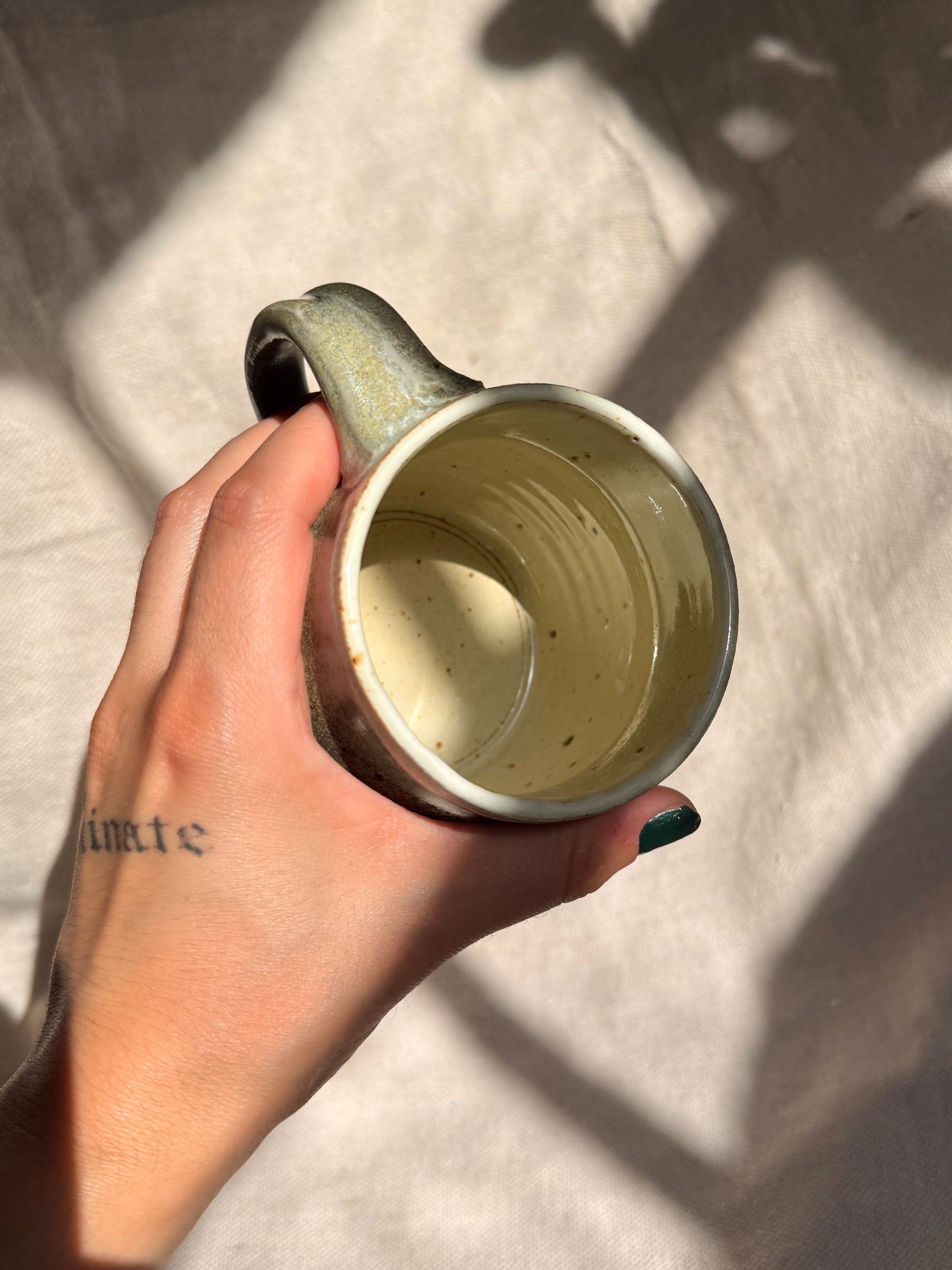 Hand holding a ceramic mug with a textured surface on a light fabric background
