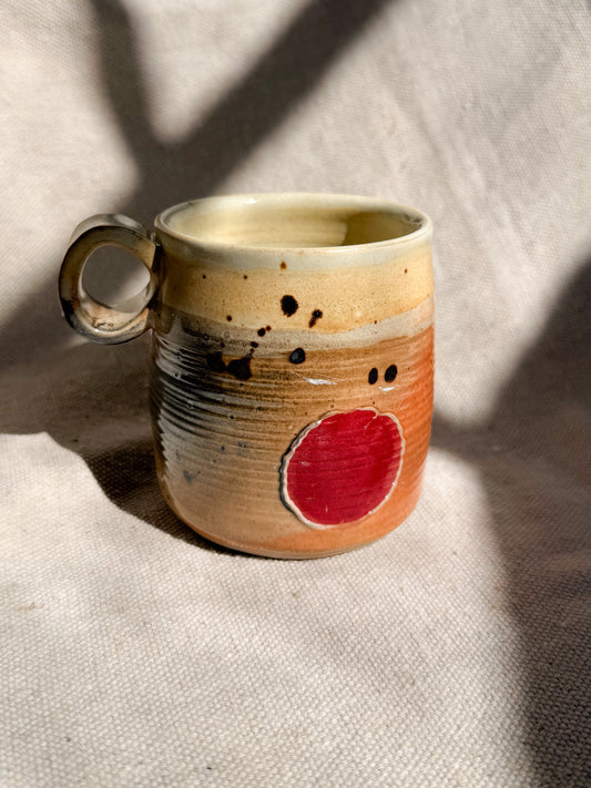 Ceramic mug with a red circle and black speckles on a textured surface