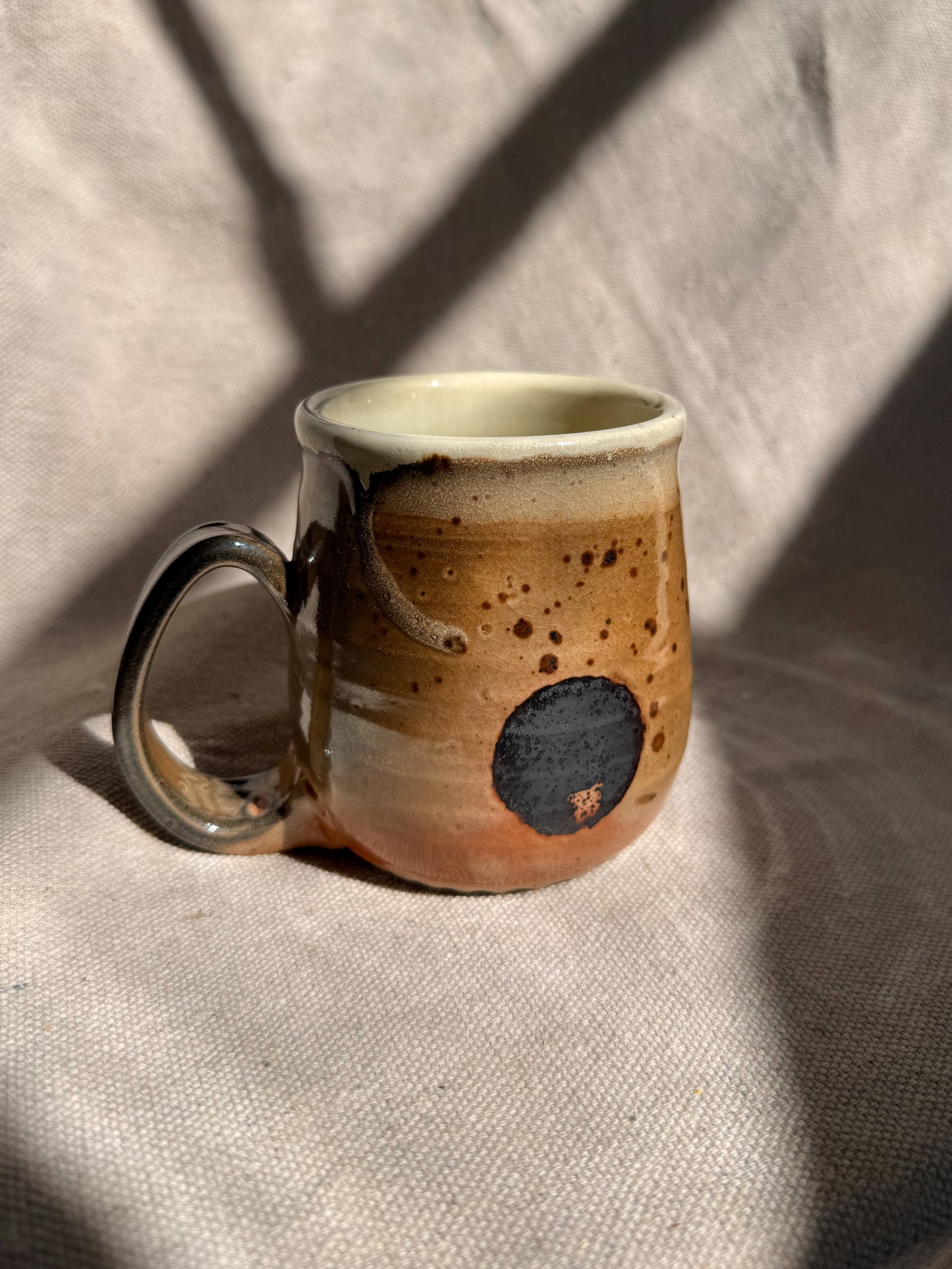 Ceramic mug with brown and beige speckled design on a textured fabric background