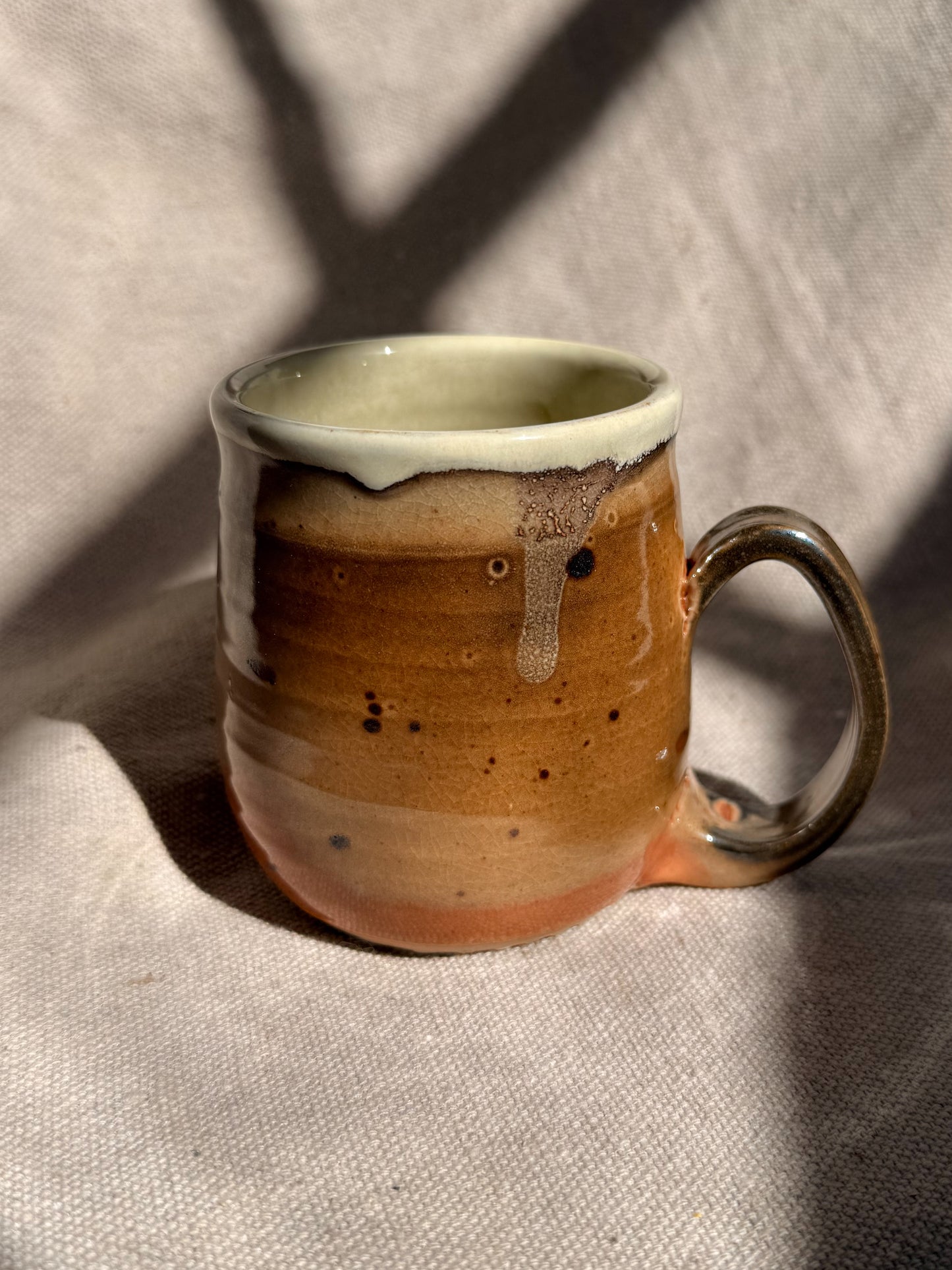 Ceramic mug with brown glaze and white rim on a textured beige background
