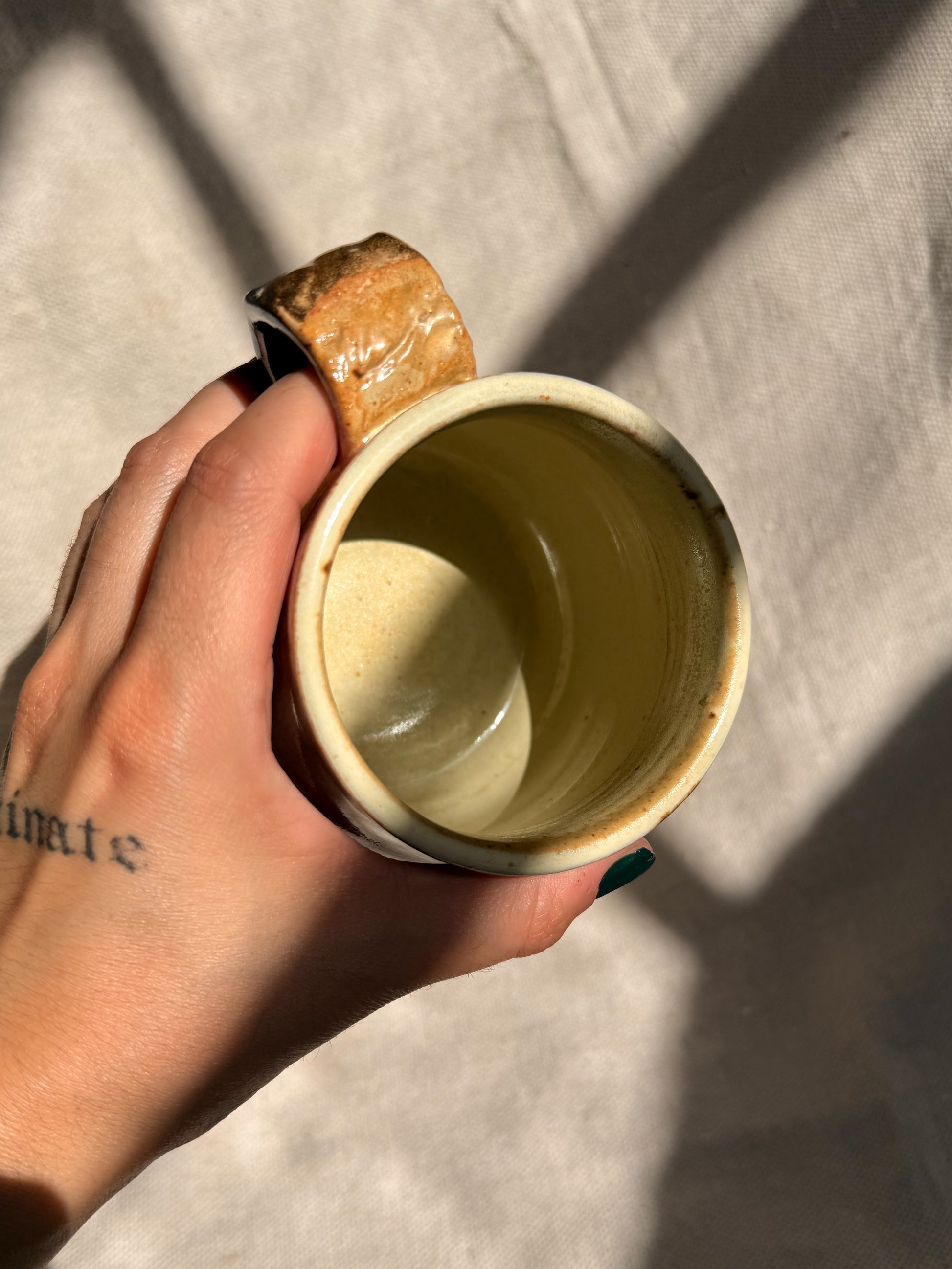 Hand holding a small ceramic cup with a wooden handle on a neutral background