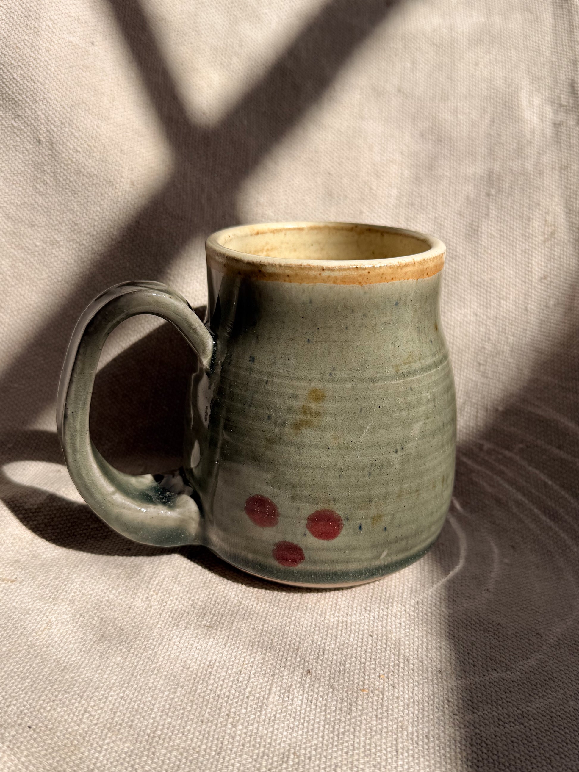 Handmade ceramic mug with a textured surface and red dots on a neutral background