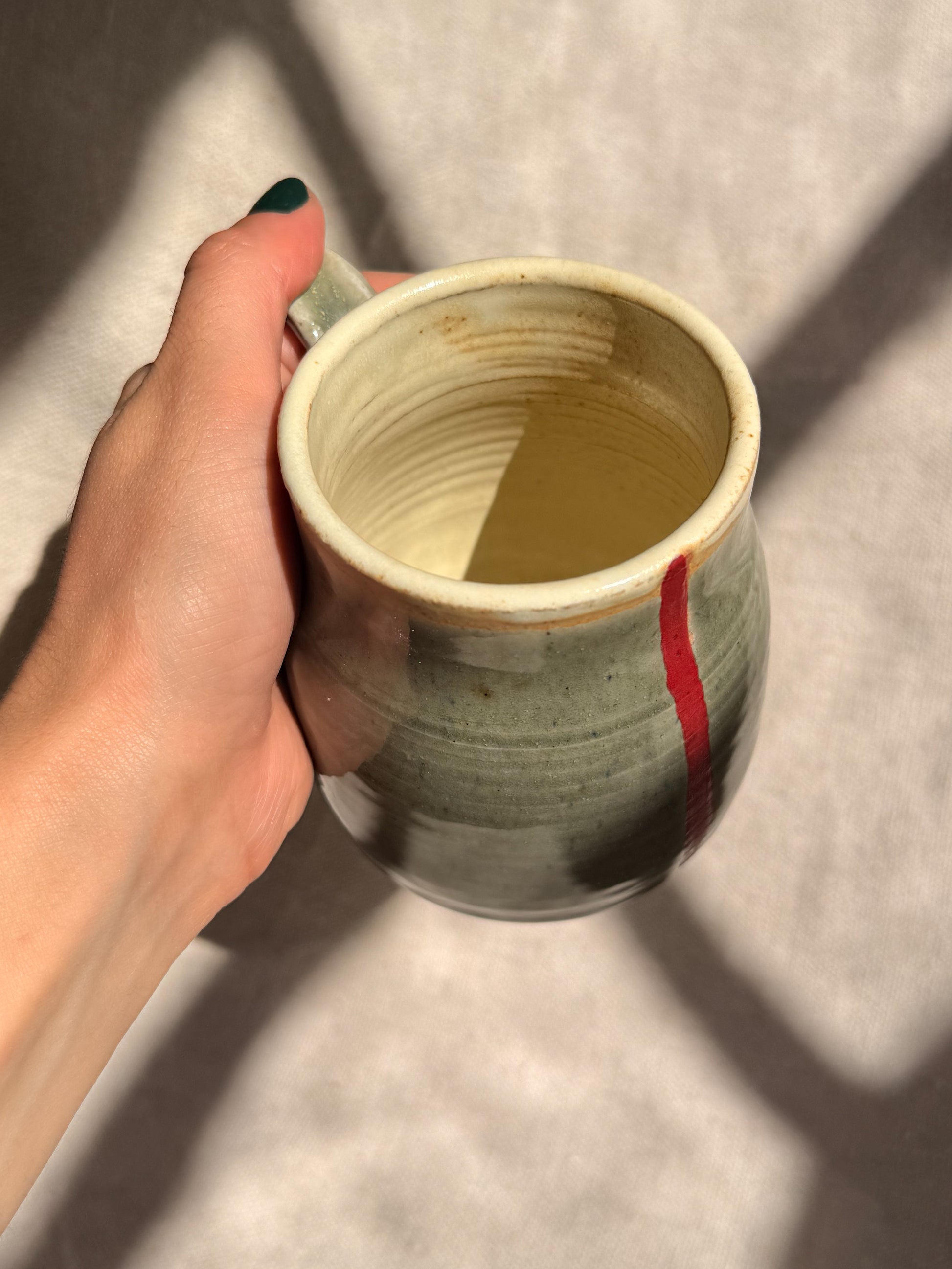 Hand holding a ceramic mug with a red accent on a neutral background