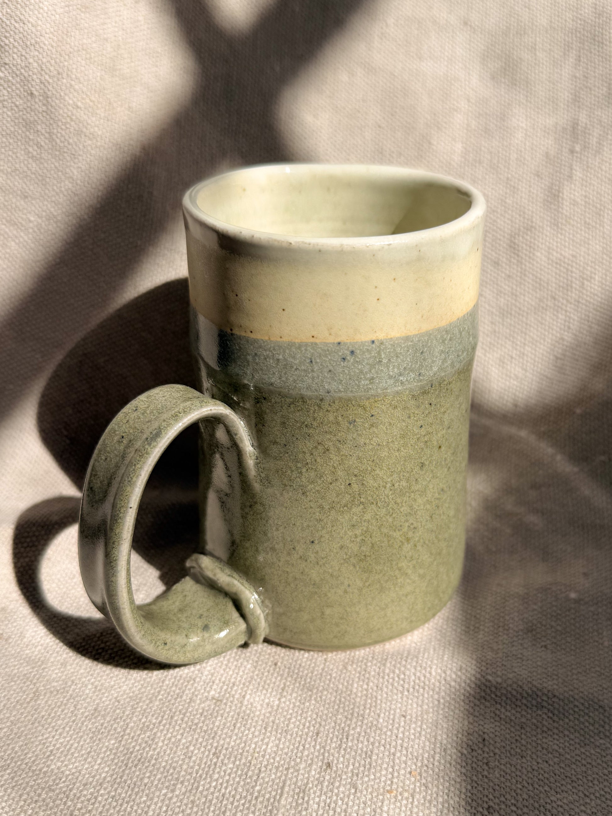 Green ceramic mug with a beige interior on a textured surface
