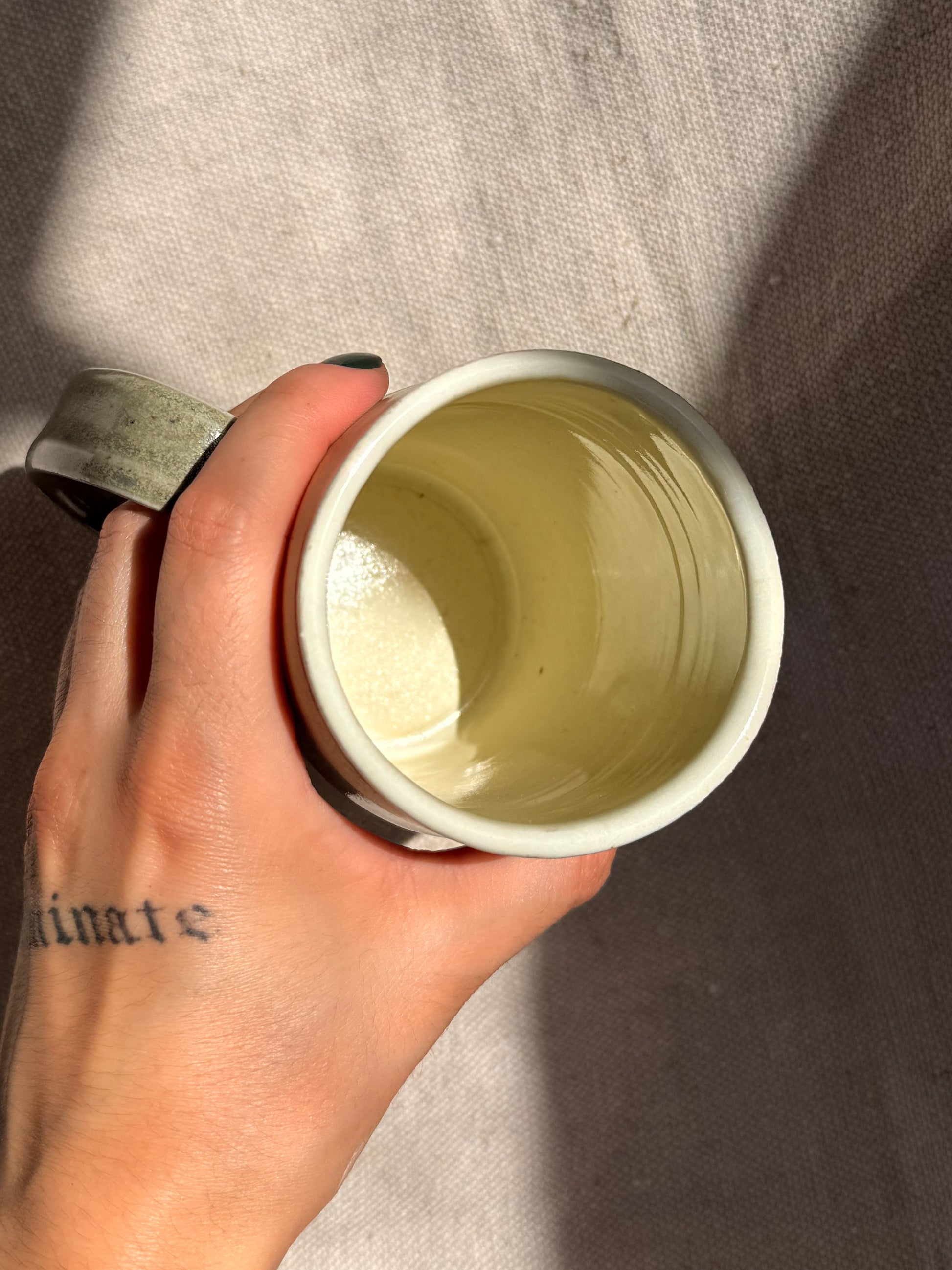 Hand holding a light green ceramic cup against a neutral background