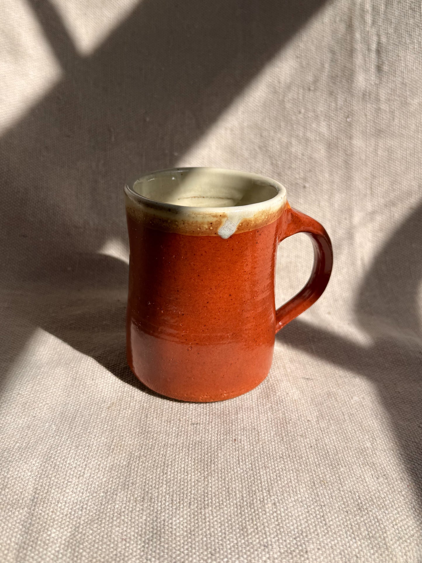 Red ceramic mug on a textured beige surface with soft shadows