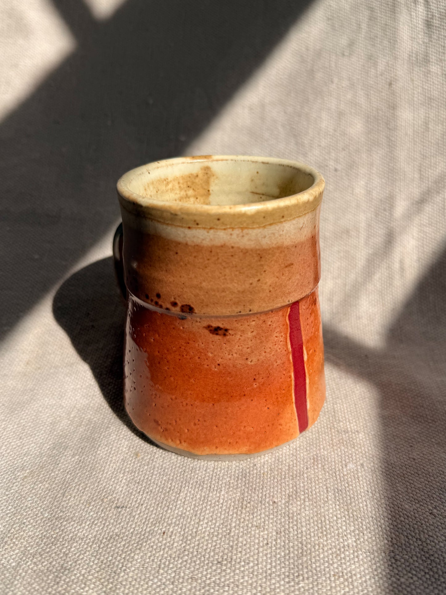 Handmade ceramic cup with a gradient from beige to red on a textured surface.