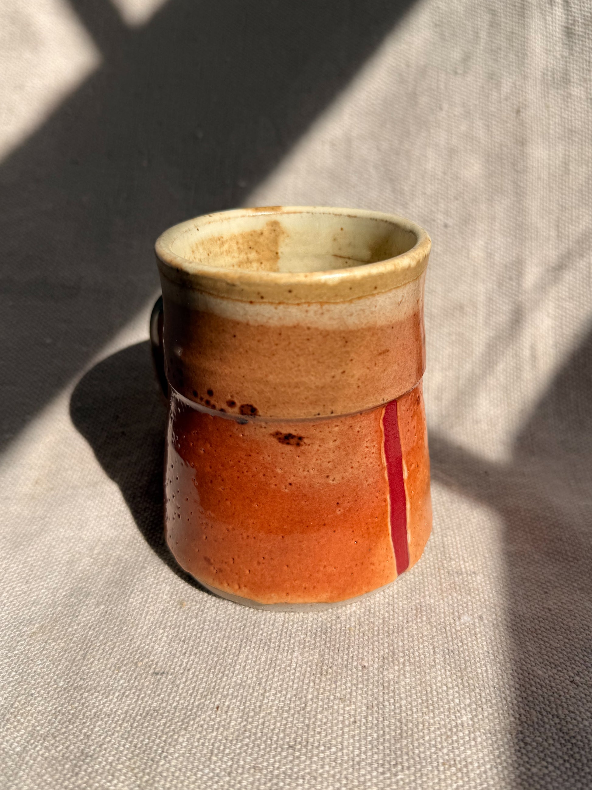 Handmade ceramic cup with a gradient from beige to red on a textured surface.