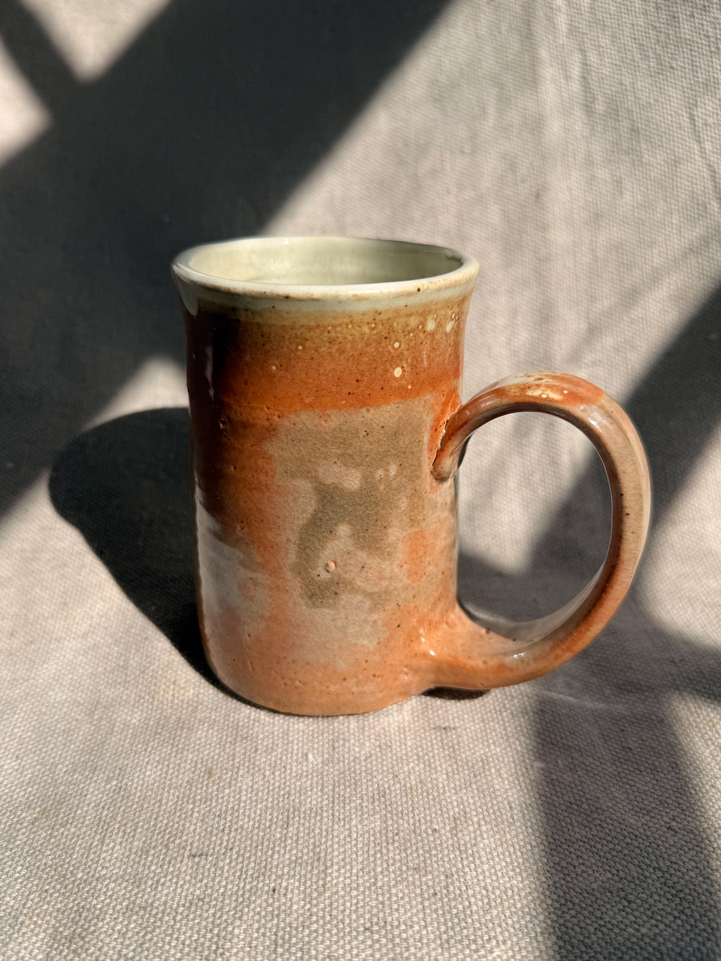 Ceramic mug with brown and beige glaze on a textured fabric background