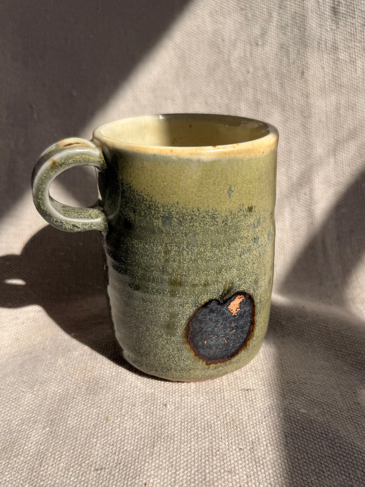 Green ceramic mug with a unique design on a textured surface