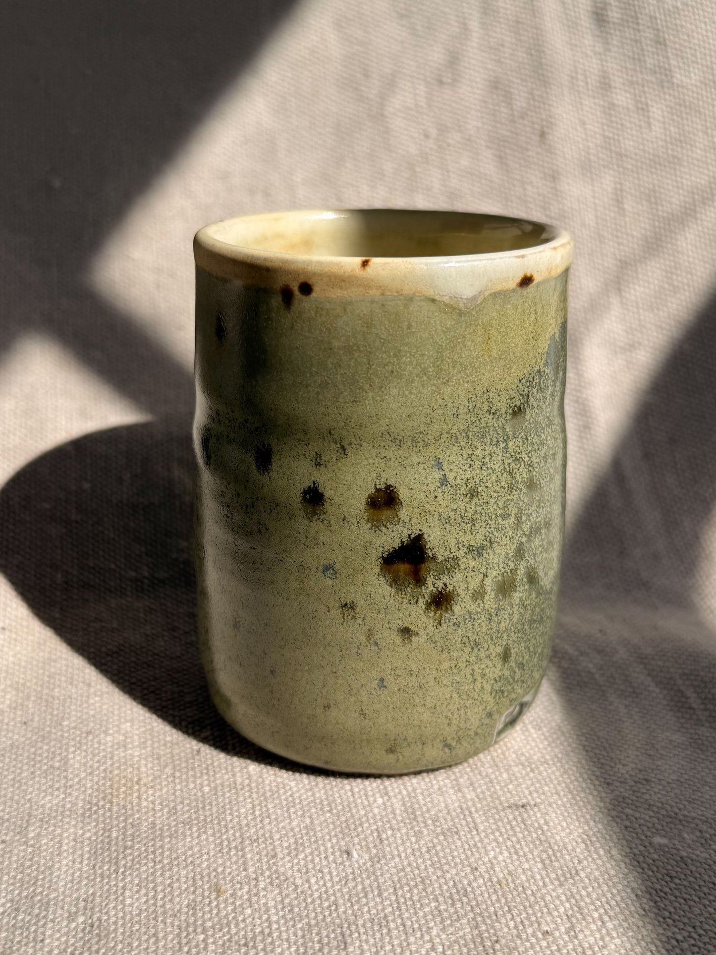 Green ceramic cup with speckled pattern on a textured surface