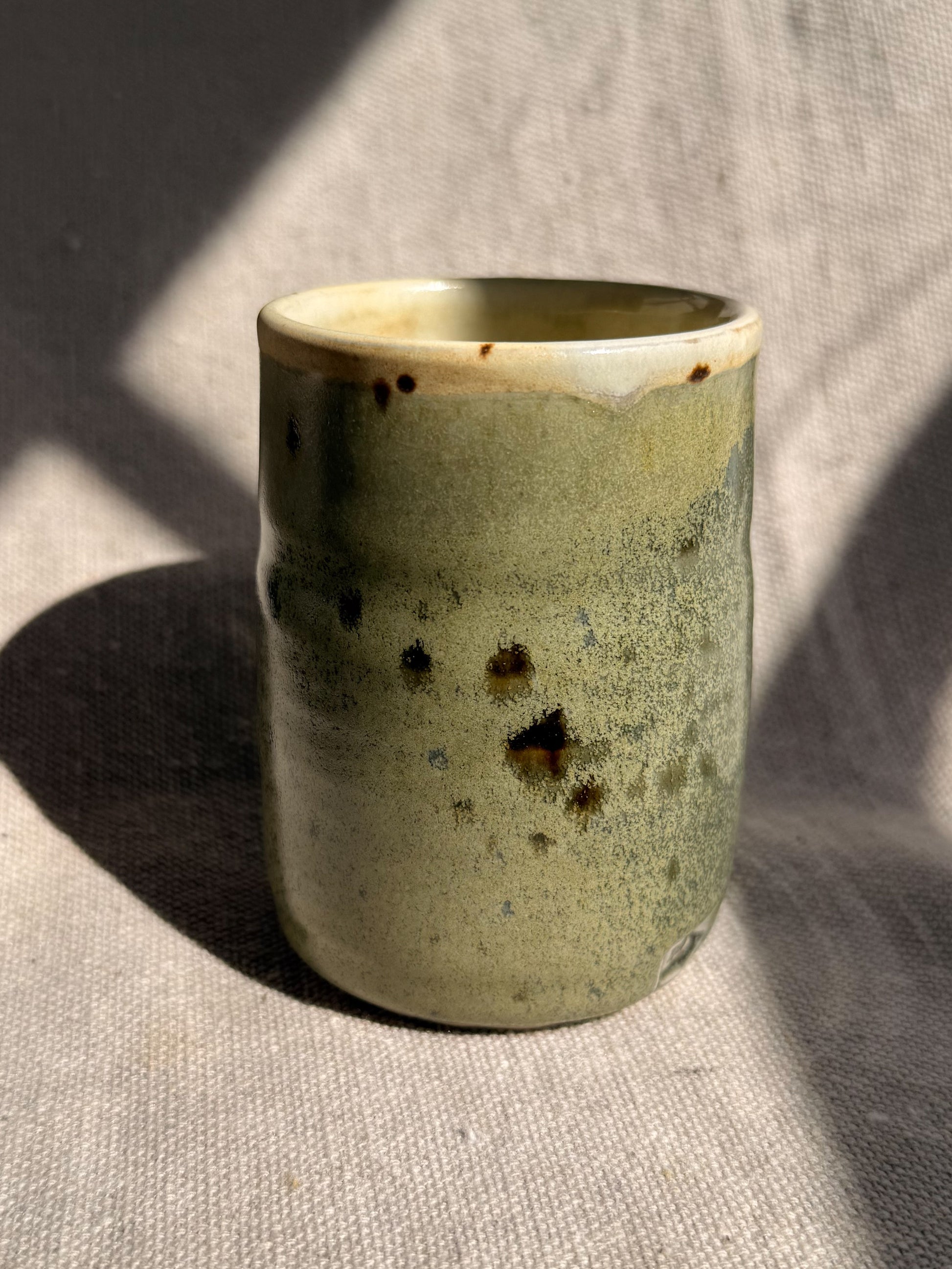 Green ceramic cup with speckled pattern on a textured surface