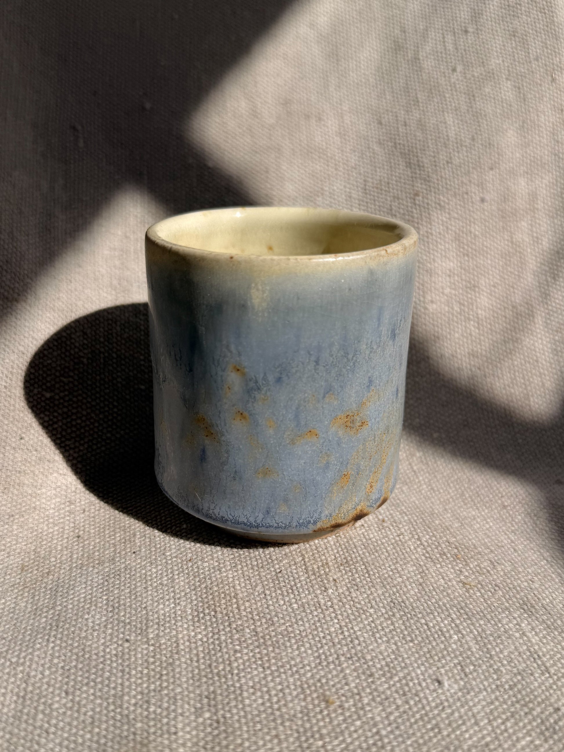 Ceramic cup with blue glaze and gold speckles on a textured surface