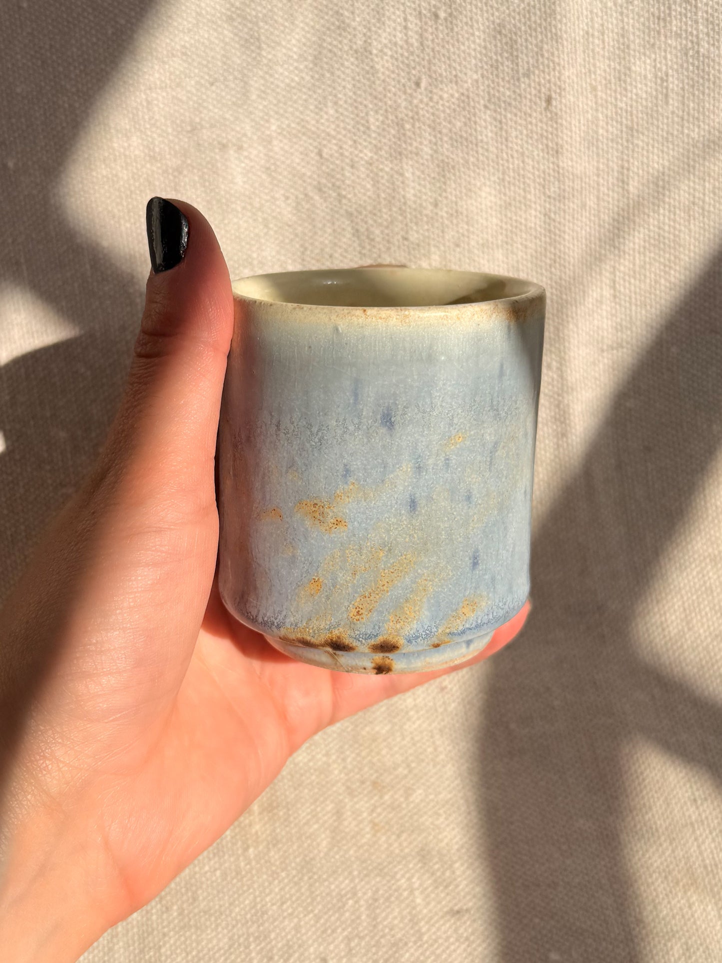 Hand holding a small ceramic cup with a textured surface against a neutral background