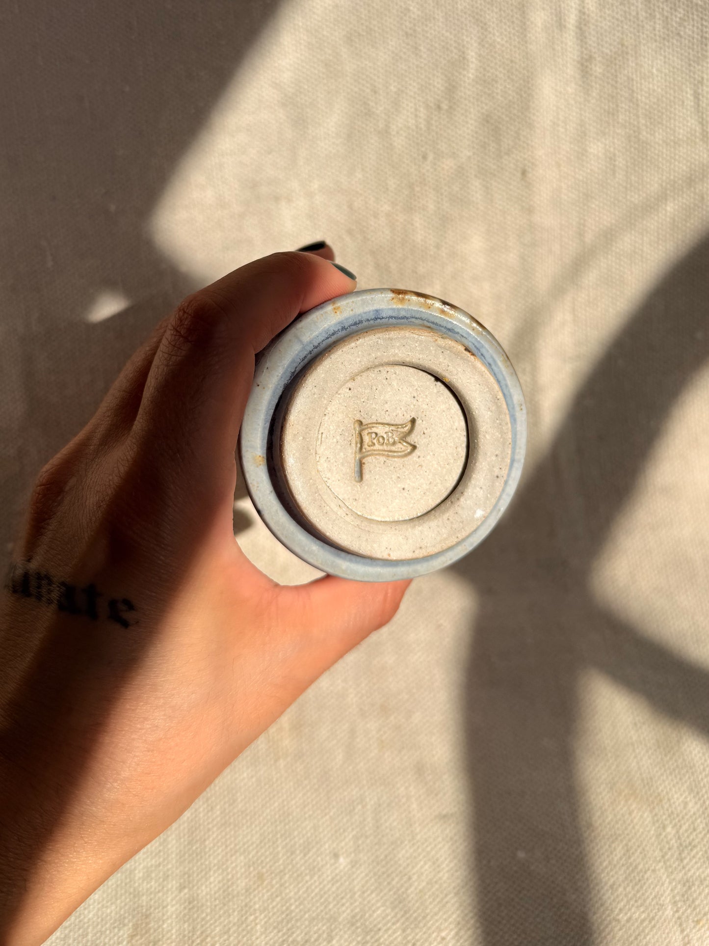 Hand holding a cylindrical object with a logo on a neutral background