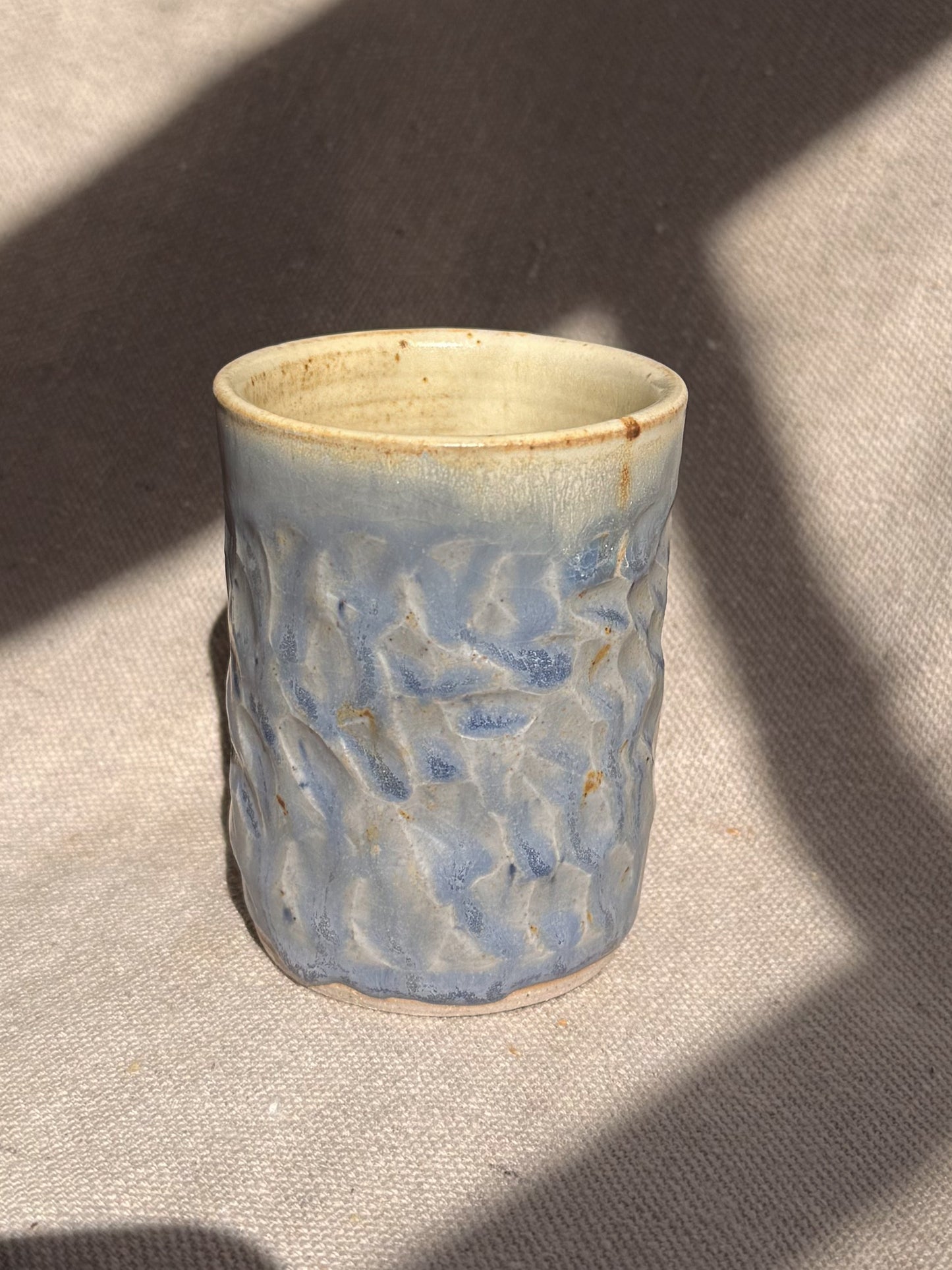 Ceramic cup with textured blue design on a beige surface