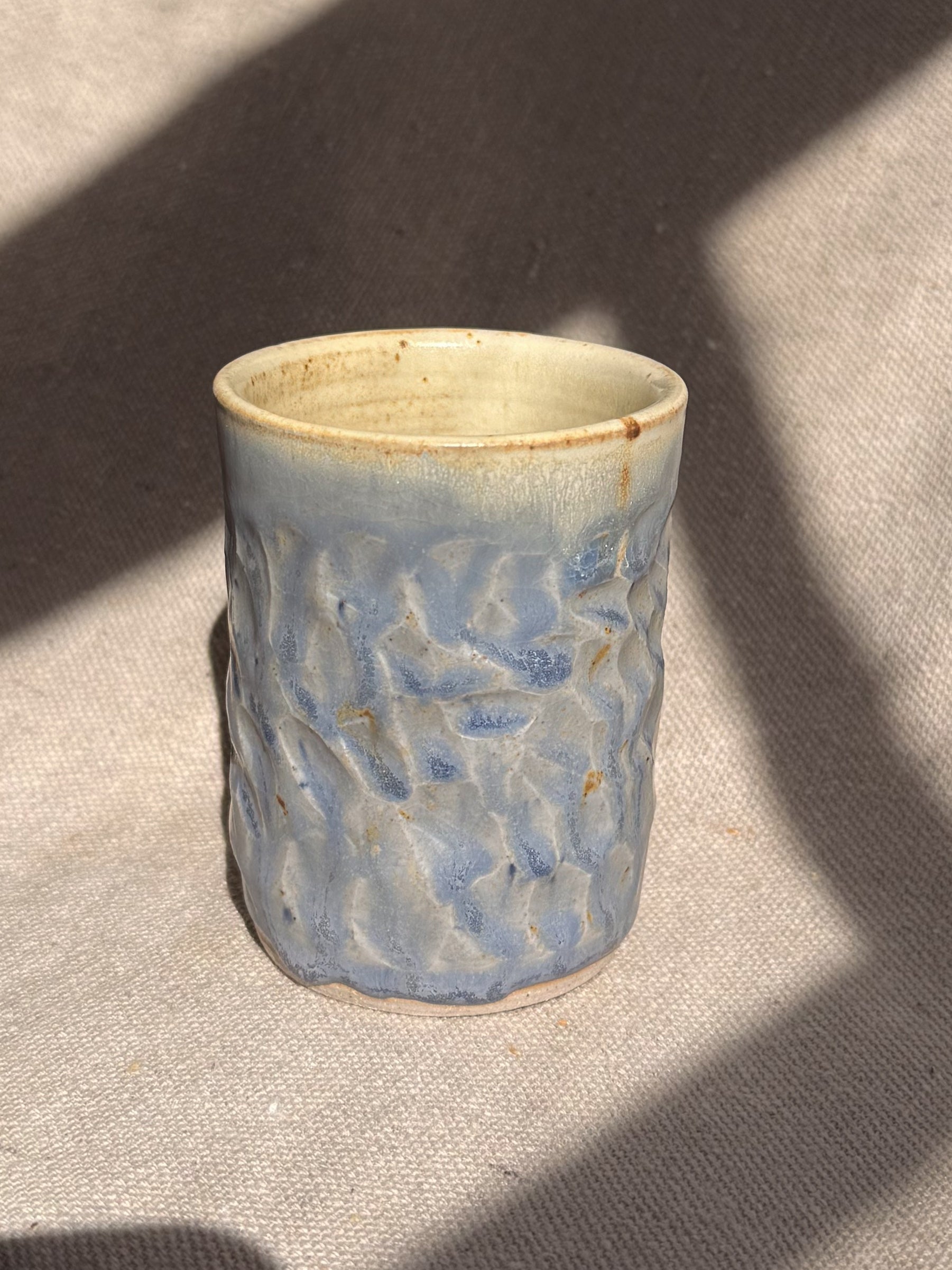 Ceramic cup with textured blue design on a beige surface