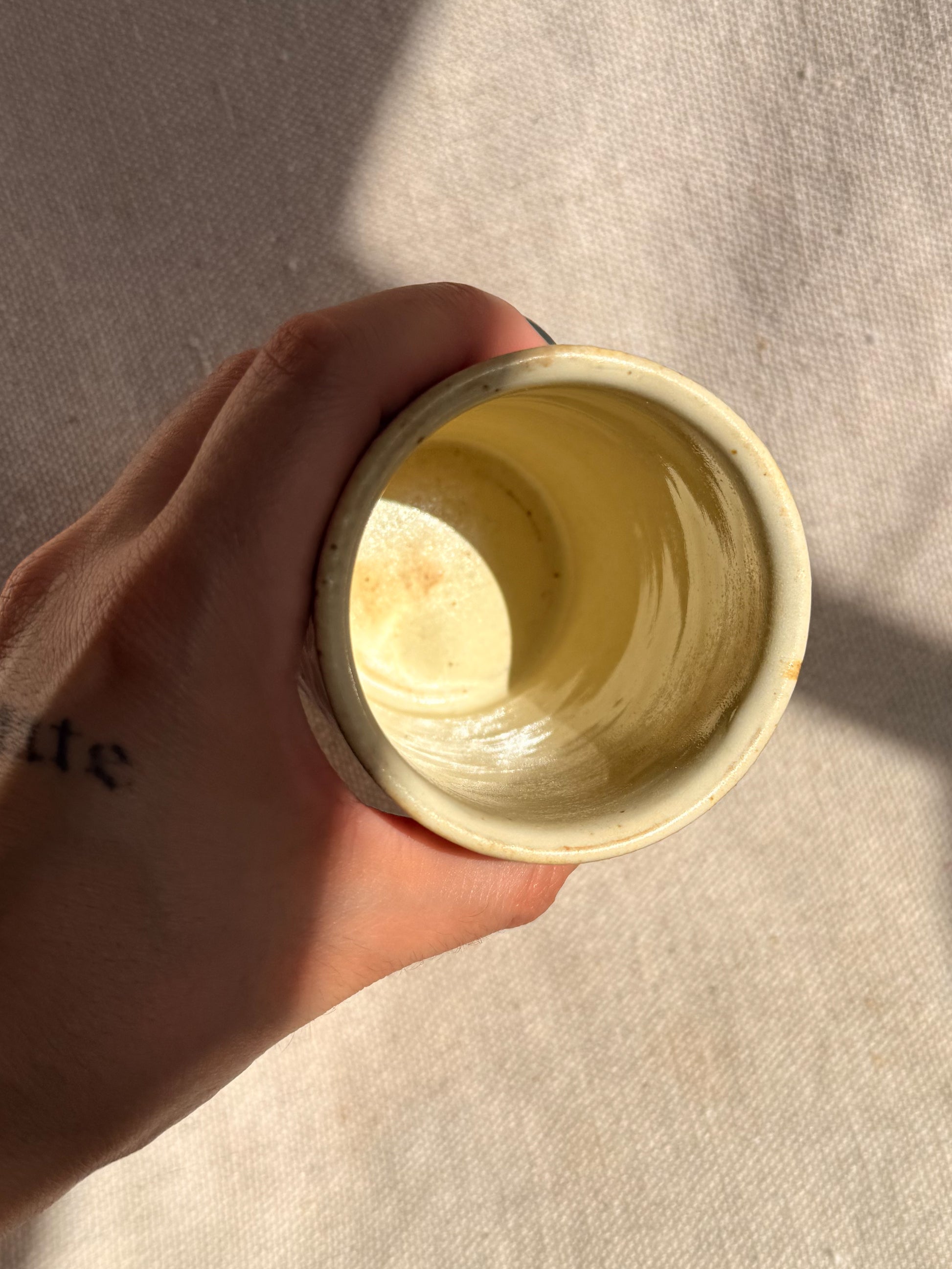 Hand holding a yellow ceramic cup against a neutral background