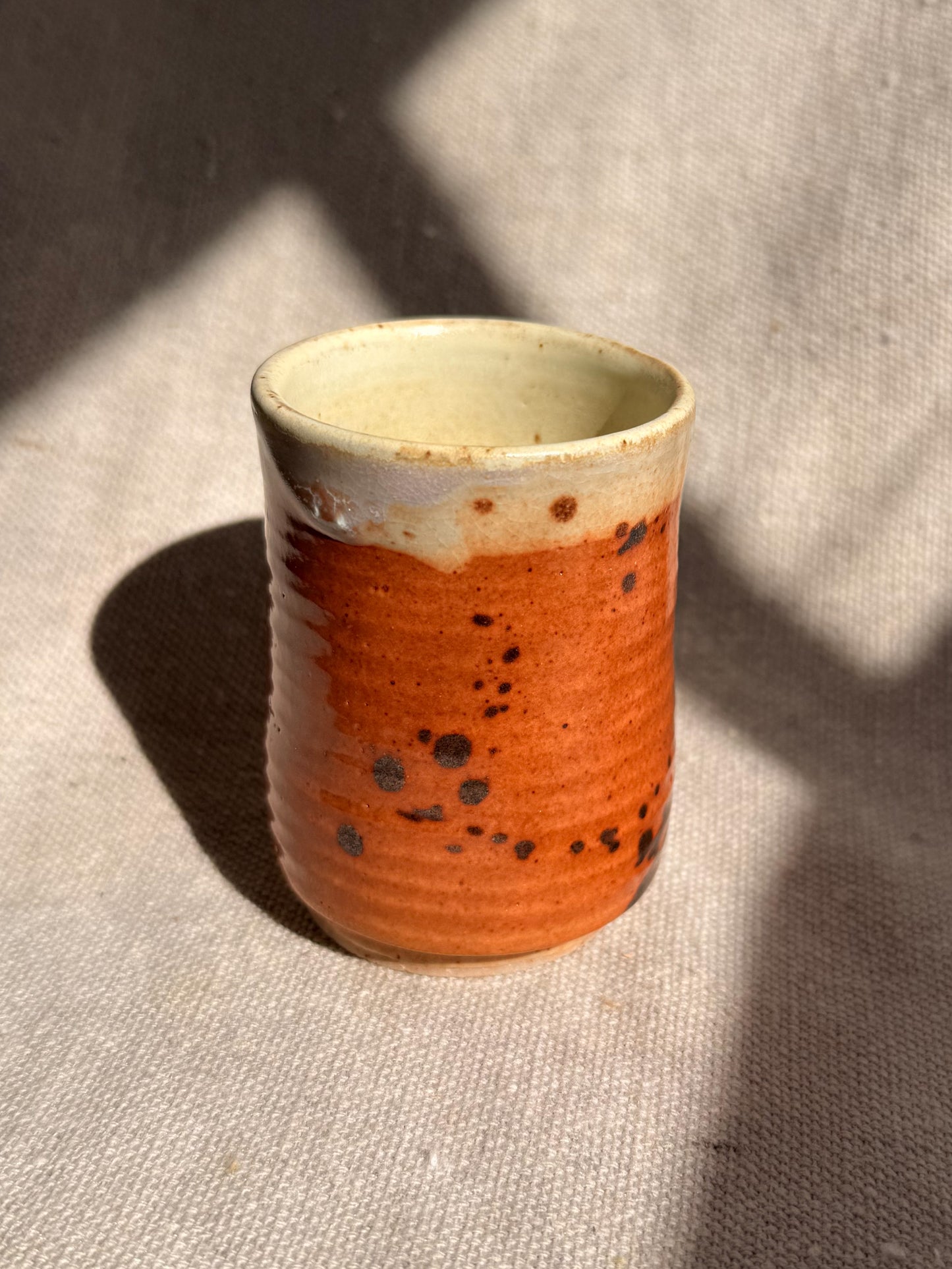 Ceramic cup with orange glaze and black speckles on a textured surface