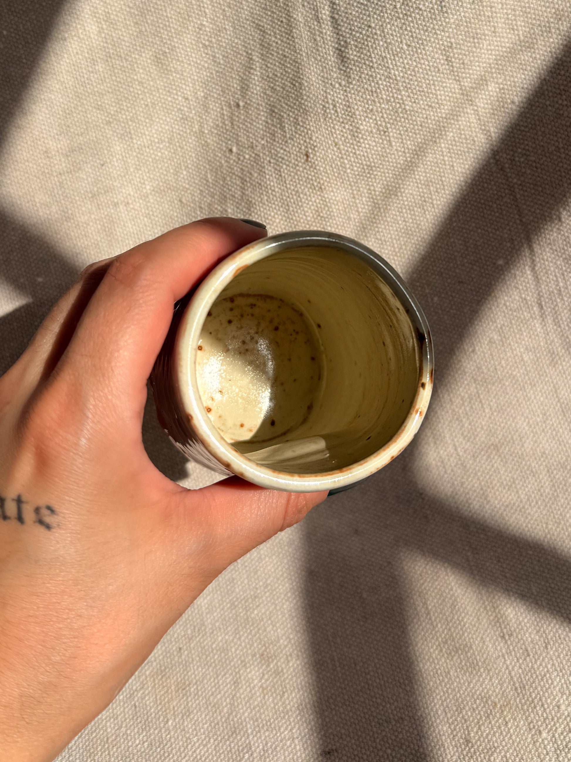 Hand holding a small ceramic cup with a textured interior against a neutral background
