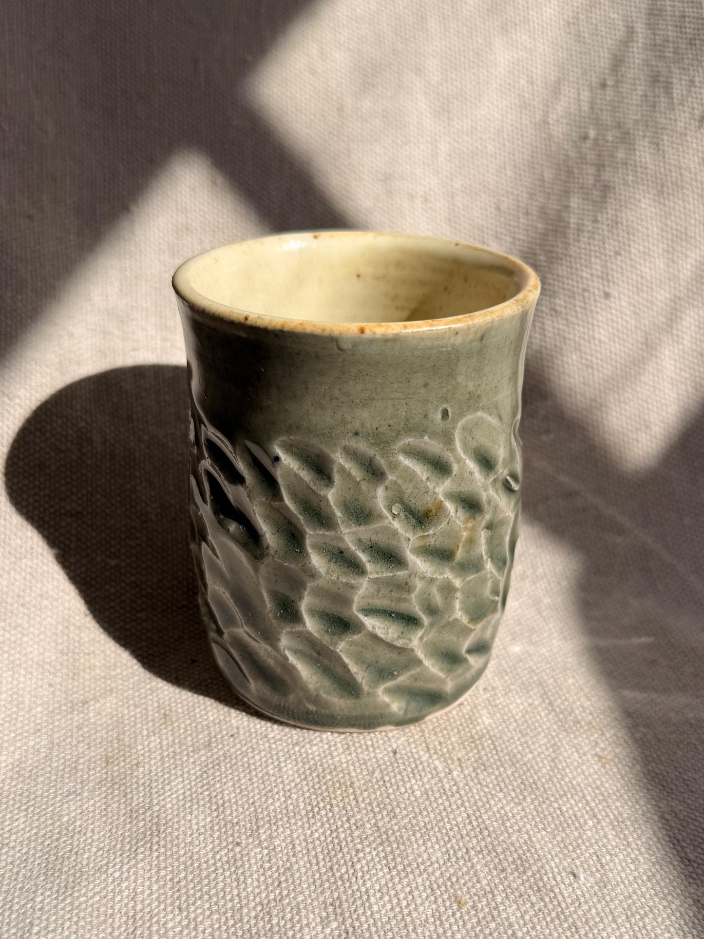 Green ceramic cup with textured design on a textured surface