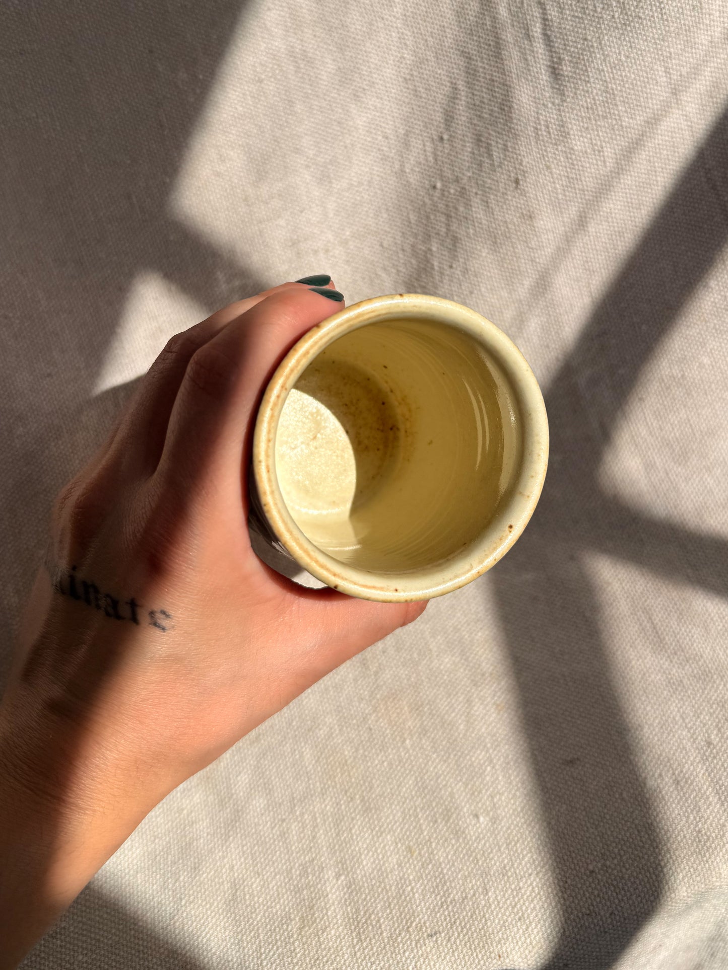 Hand holding a small yellow cup against a neutral background
