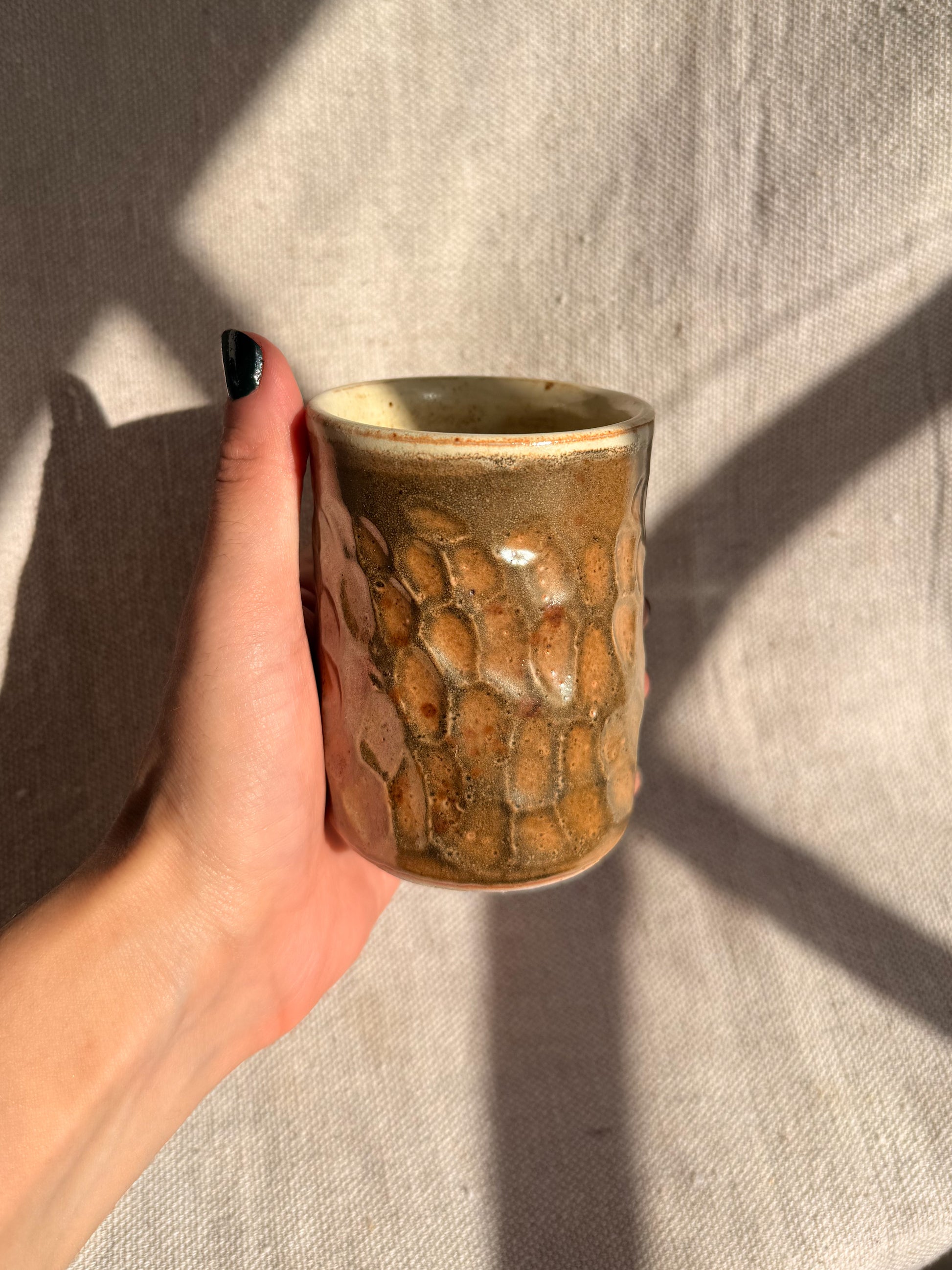 Hand holding a textured ceramic cup against a neutral background