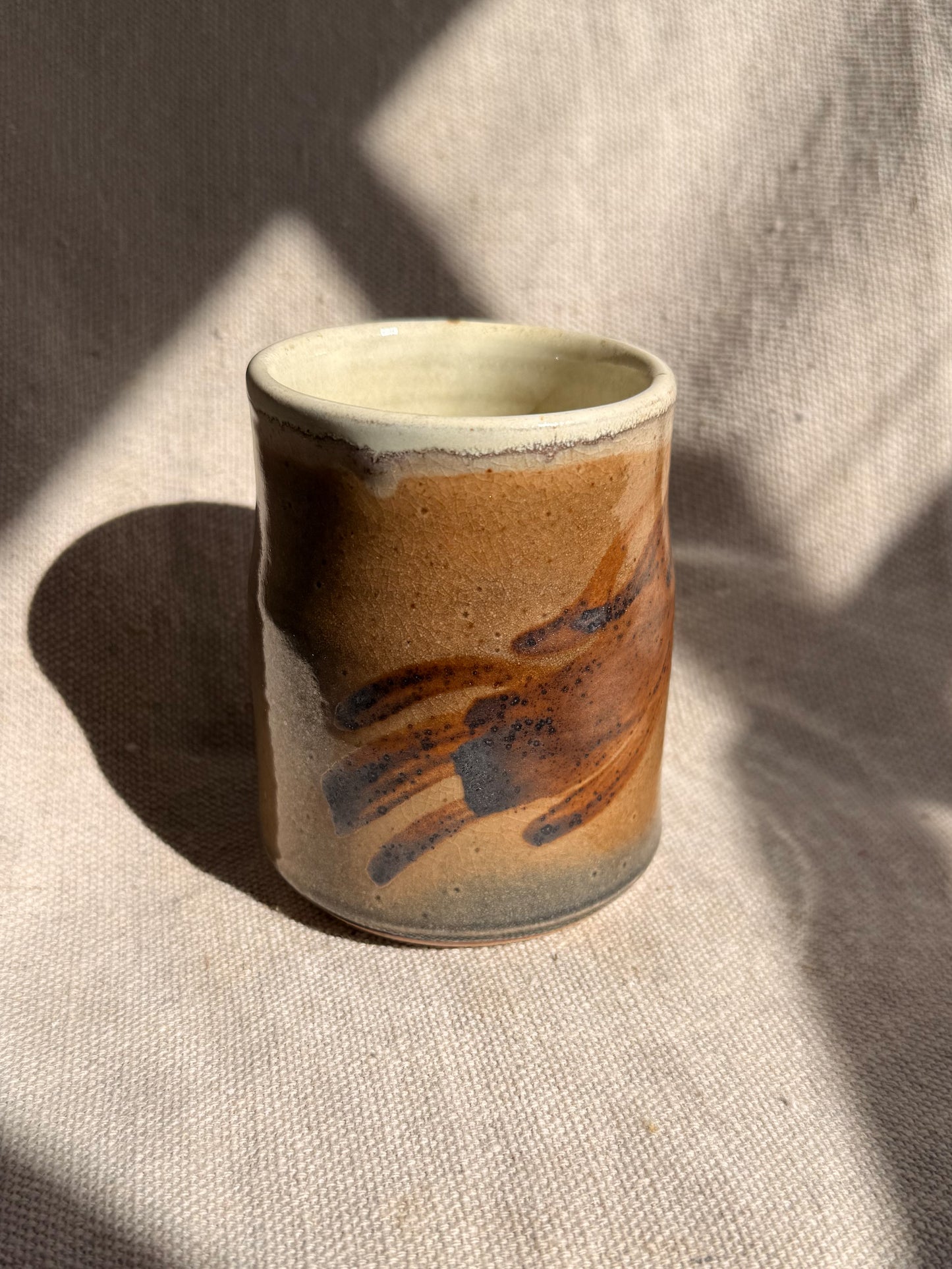 Ceramic cup with brown and black glaze on a textured beige surface