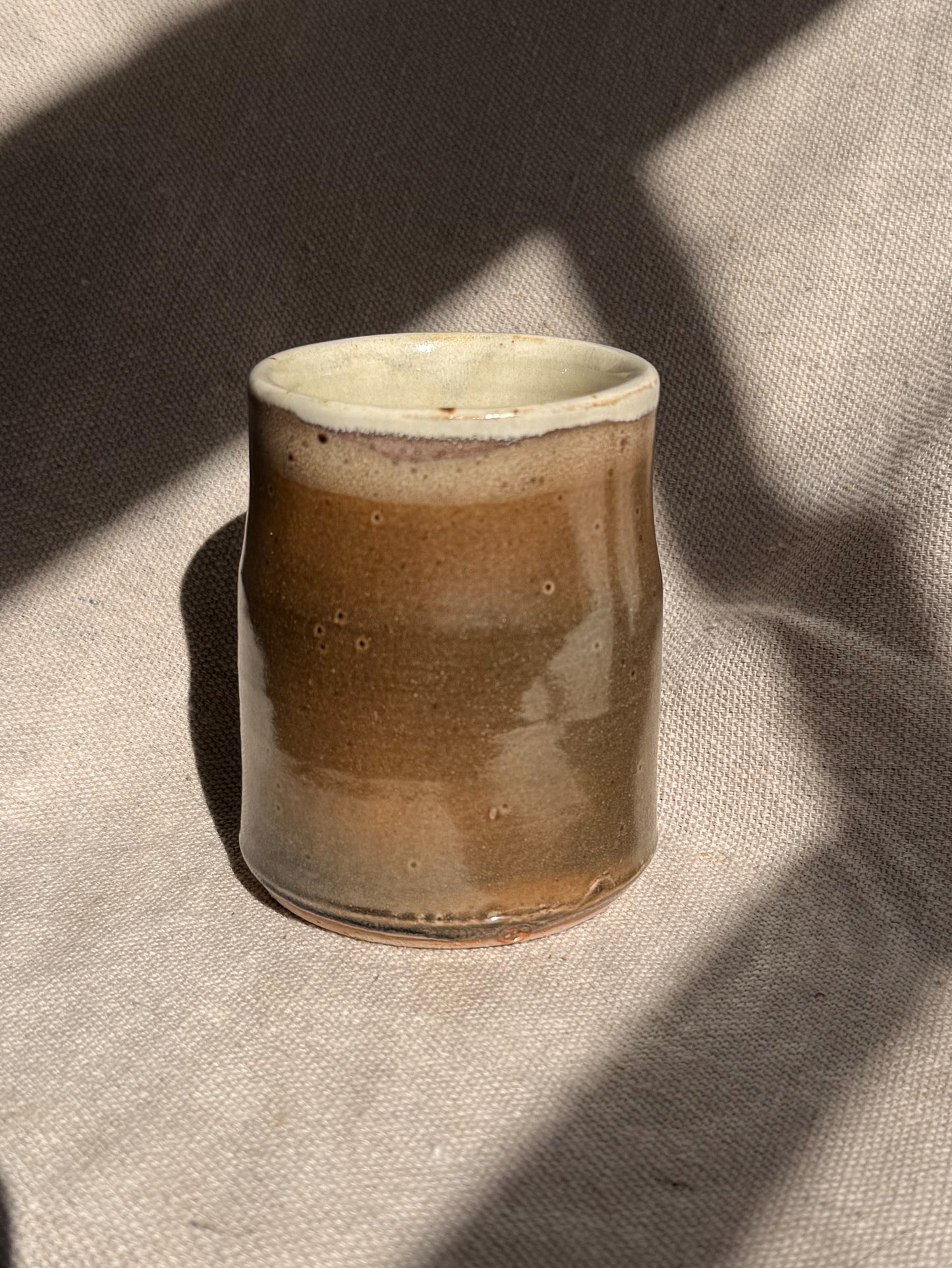 Ceramic cup with brown glaze on a textured beige surface