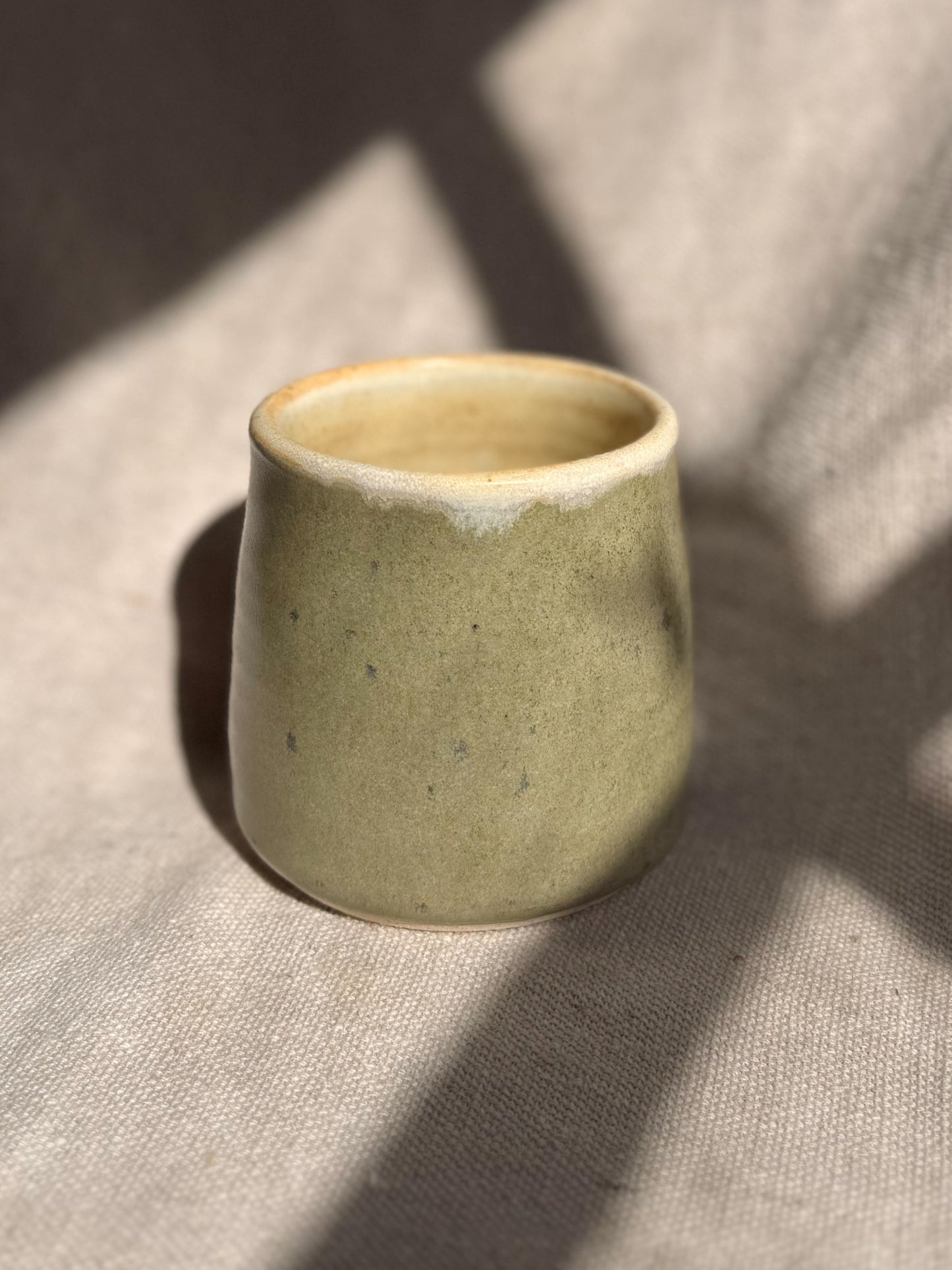 Green ceramic cup on a textured beige surface
