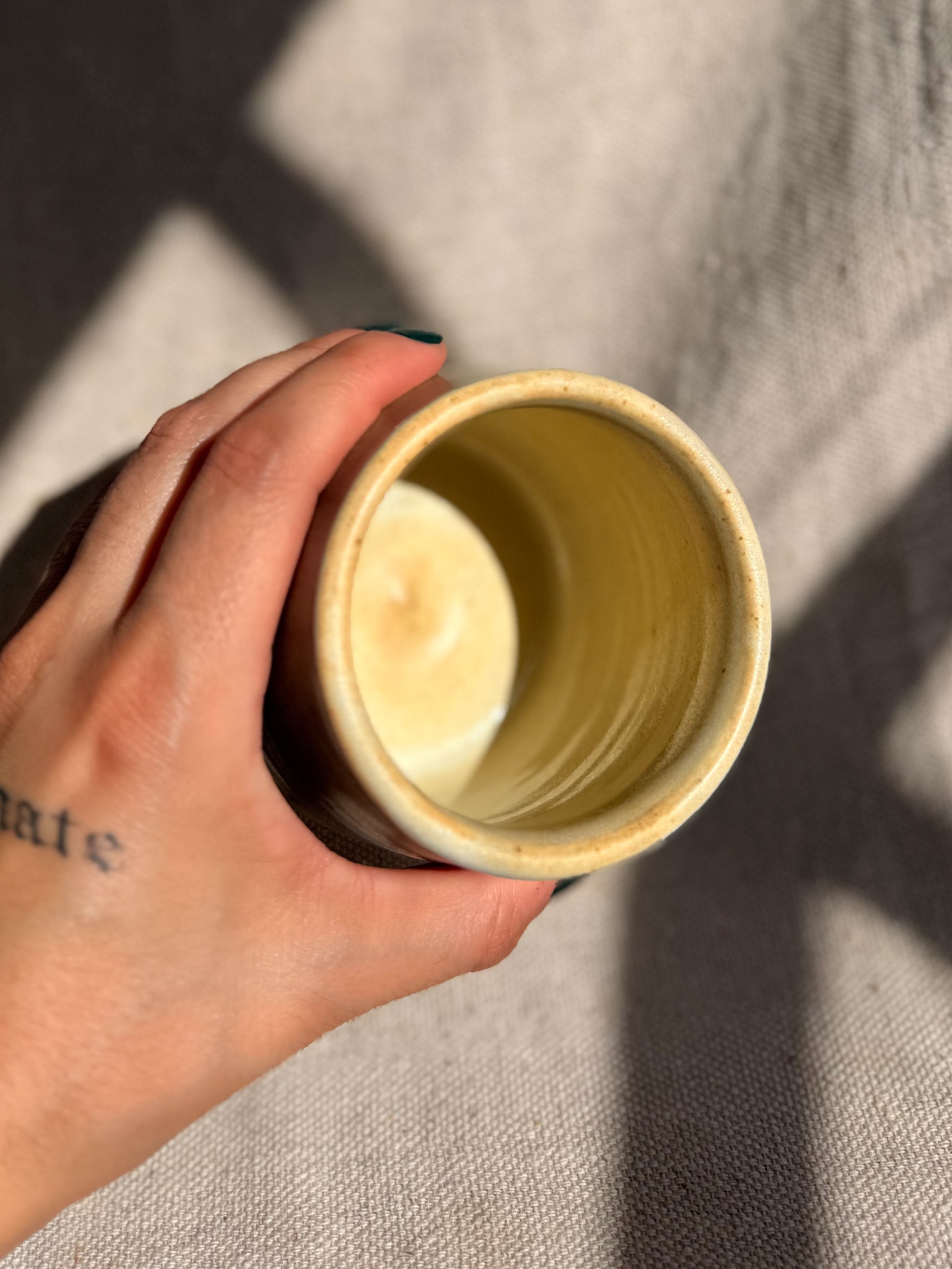 Hand holding a cylindrical beige object against a neutral background
