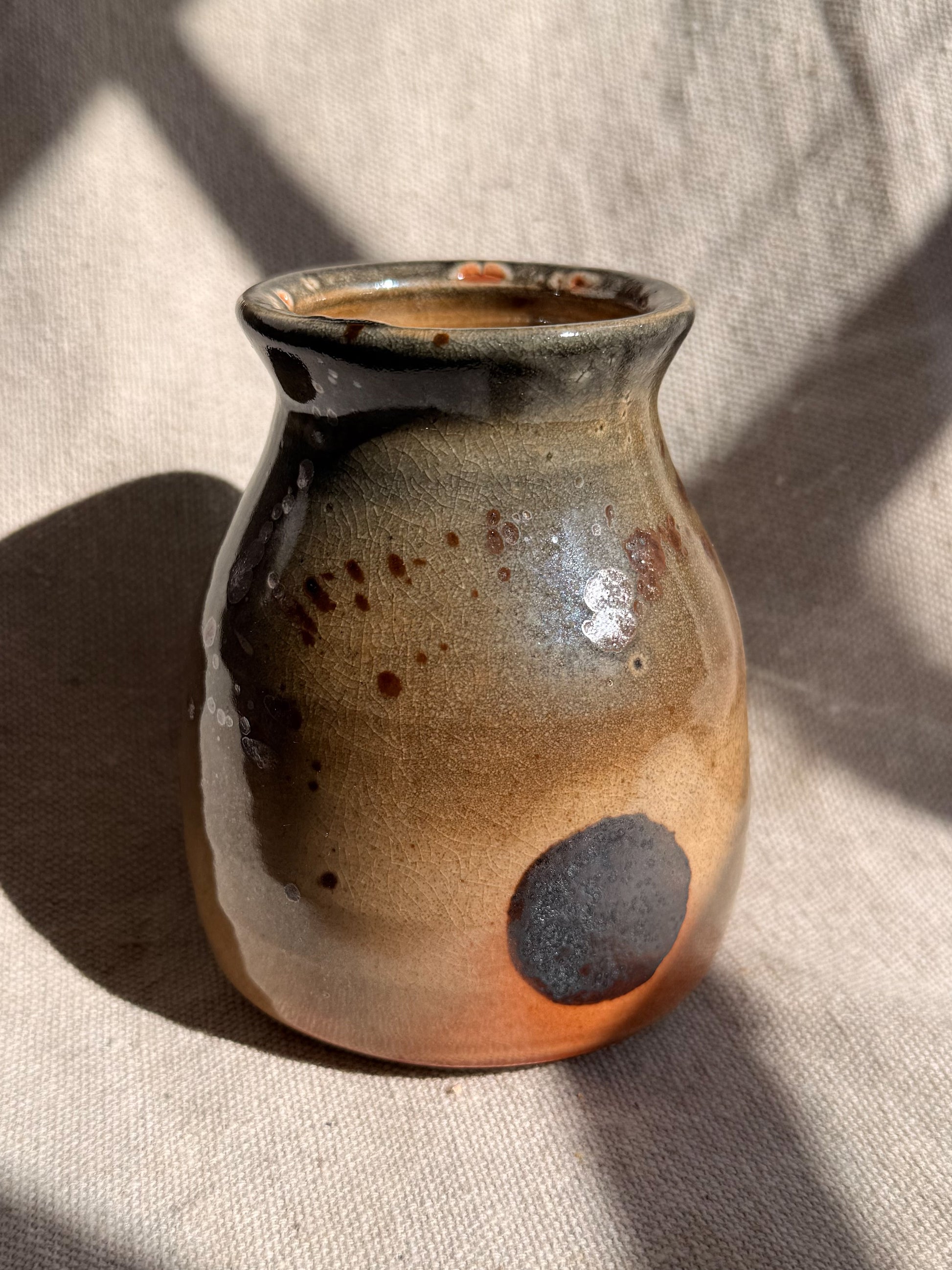 Ceramic vase with brown and gray glaze on a beige fabric background