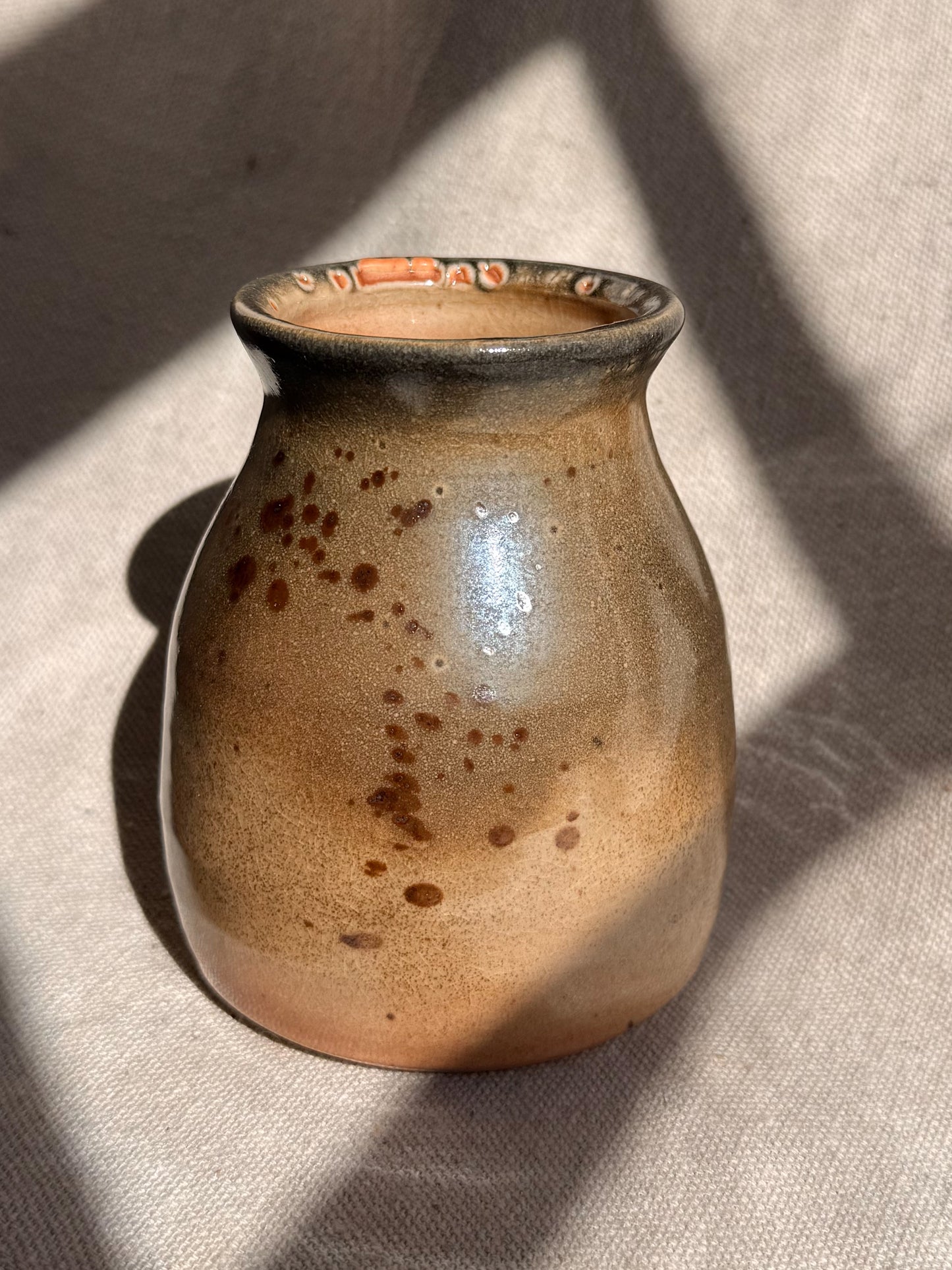 Brown ceramic vase with speckled pattern on a textured surface