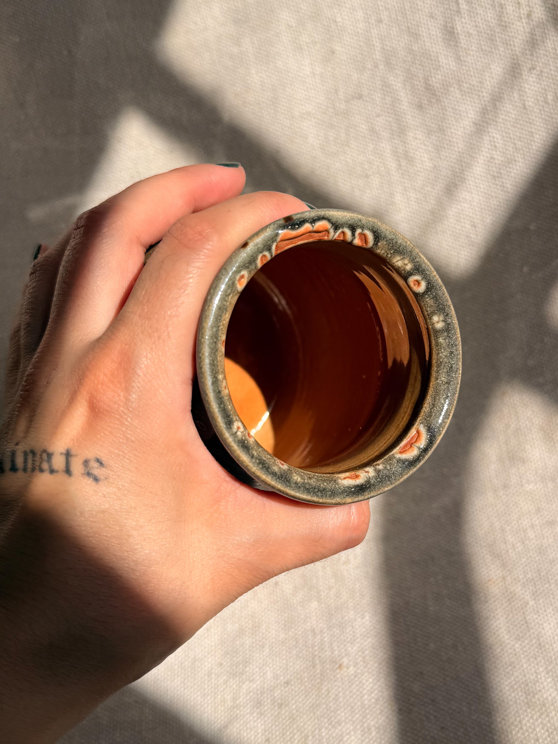Hand holding a cylindrical metal object with a worn surface against a neutral background