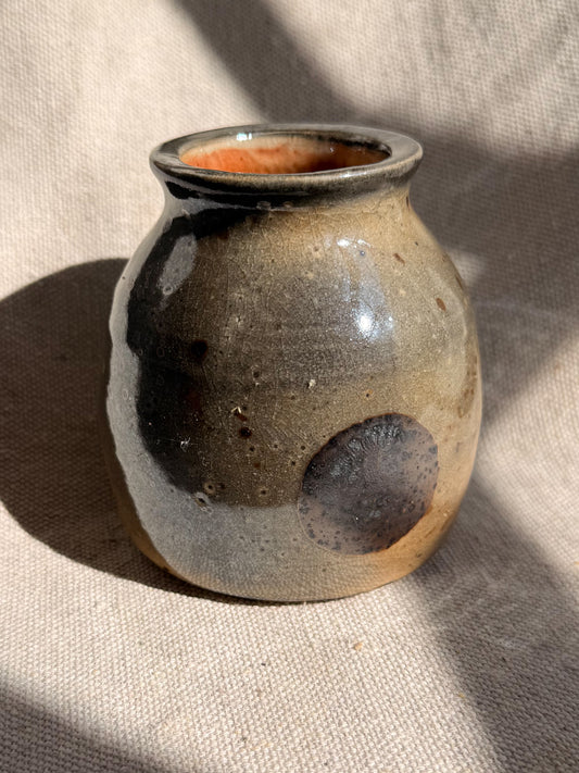 Ceramic vase with brown and black glaze on a beige fabric background
