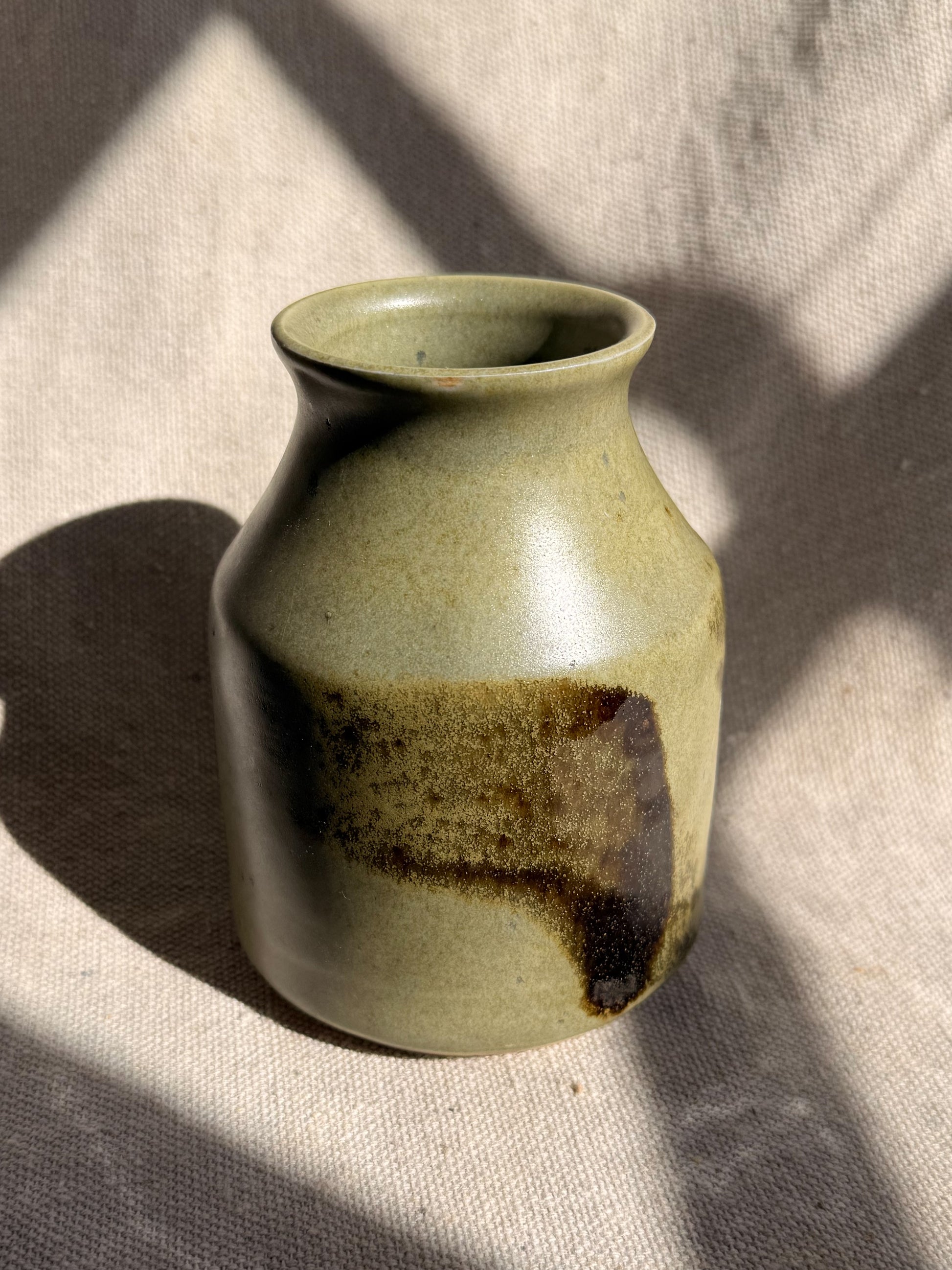 Green ceramic vase with brown accents on a textured beige surface