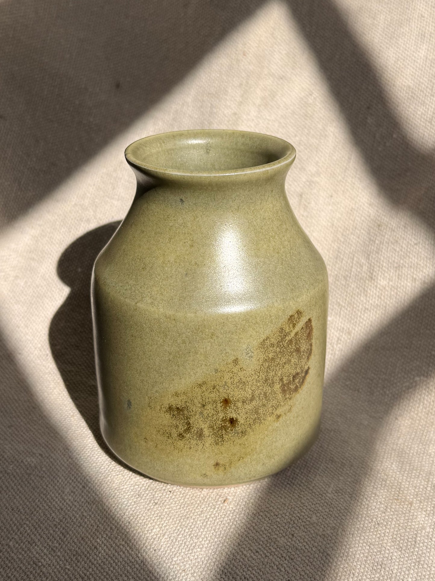 Green ceramic vase on a textured beige surface