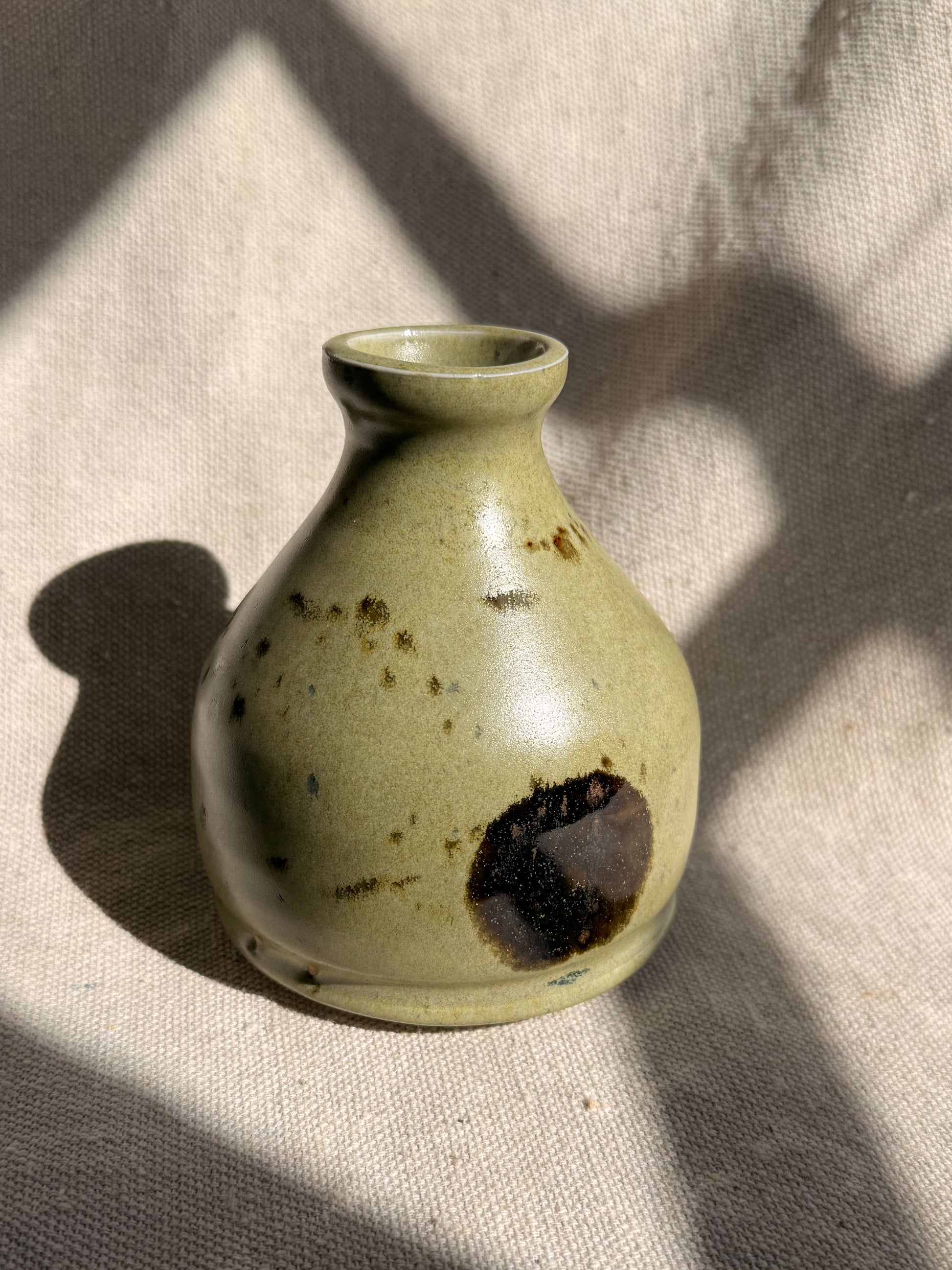 Small ceramic vase with brown speckles on a textured beige surface