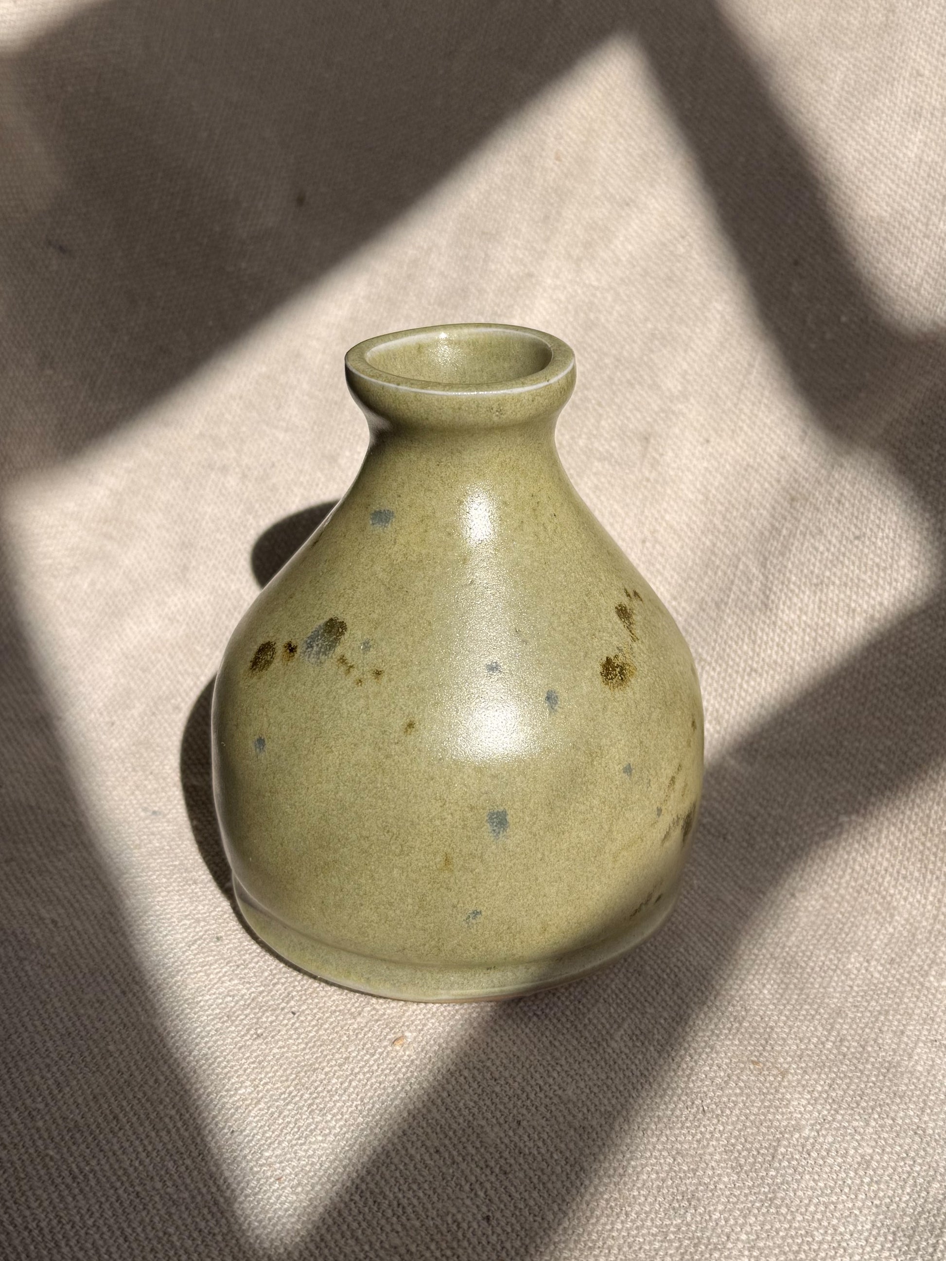 Small green ceramic vase on a textured surface with shadows