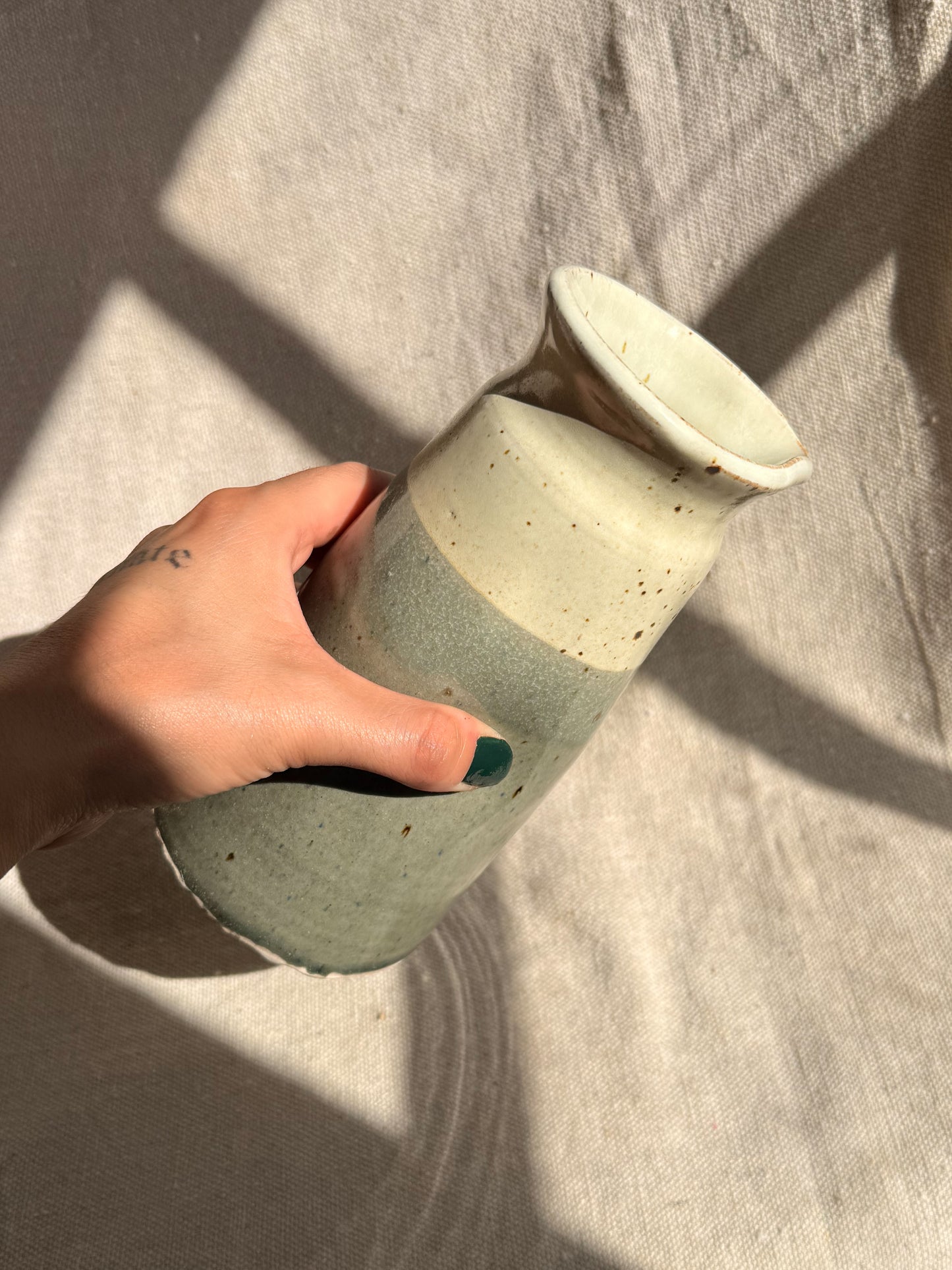Hand holding a ceramic vase with a textured surface on a neutral background